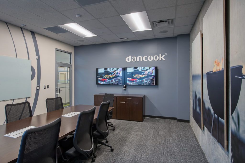 A conference room with a long table and chairs and two televisions on the wall.