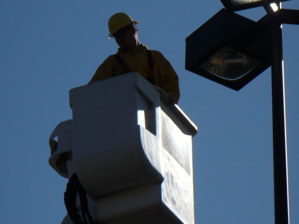 A man wearing a hard hat is working on a street light