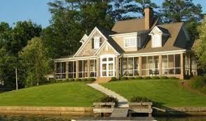 A large house is sitting on top of a grassy hill next to a body of water.