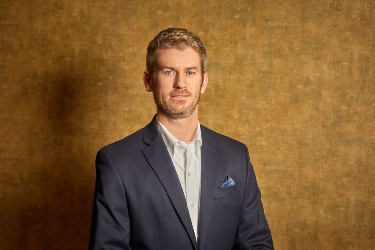 A man in a suit and tie is standing in front of a gold wall.