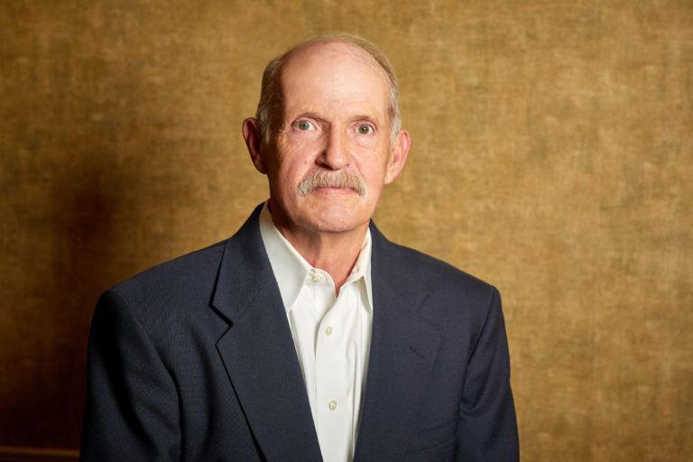 A man with a mustache is wearing a blue suit and white shirt.