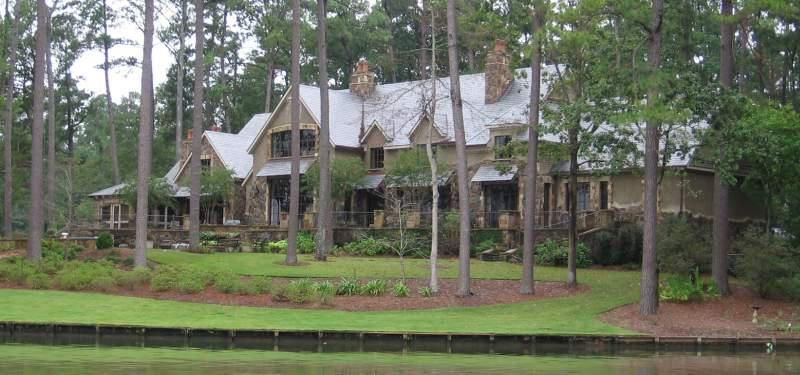 A large house is surrounded by trees next to a body of water.