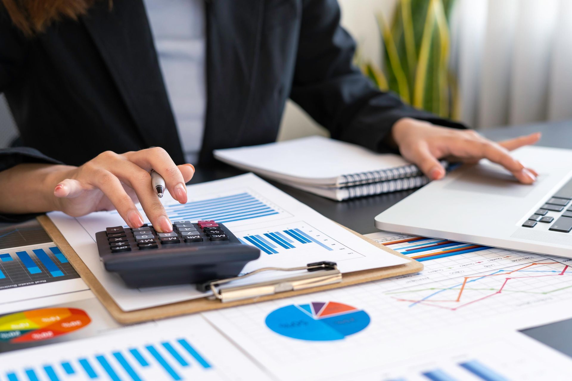 Person using a calculator and laptop over financial charts and graphs on a desk