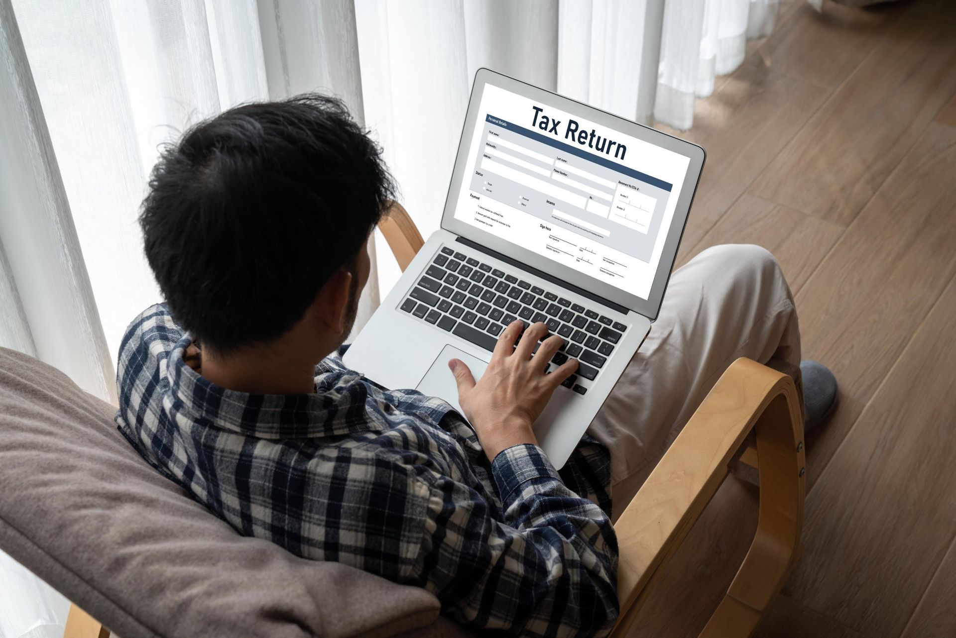 Person using a laptop in a bright window seat, with a tax return form open on the screen
