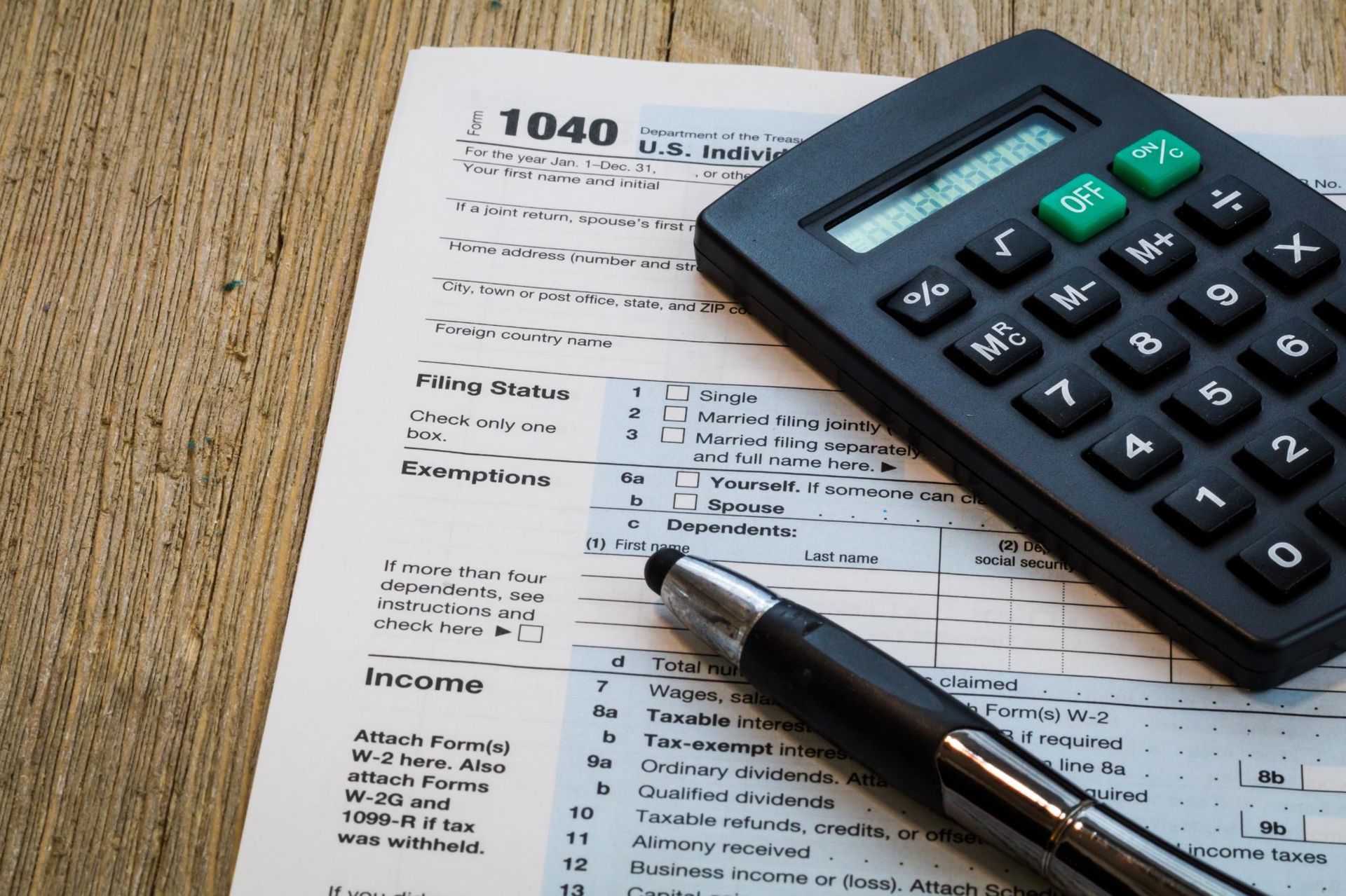 Calculator, pen, and 1040 tax form on a wooden desk.