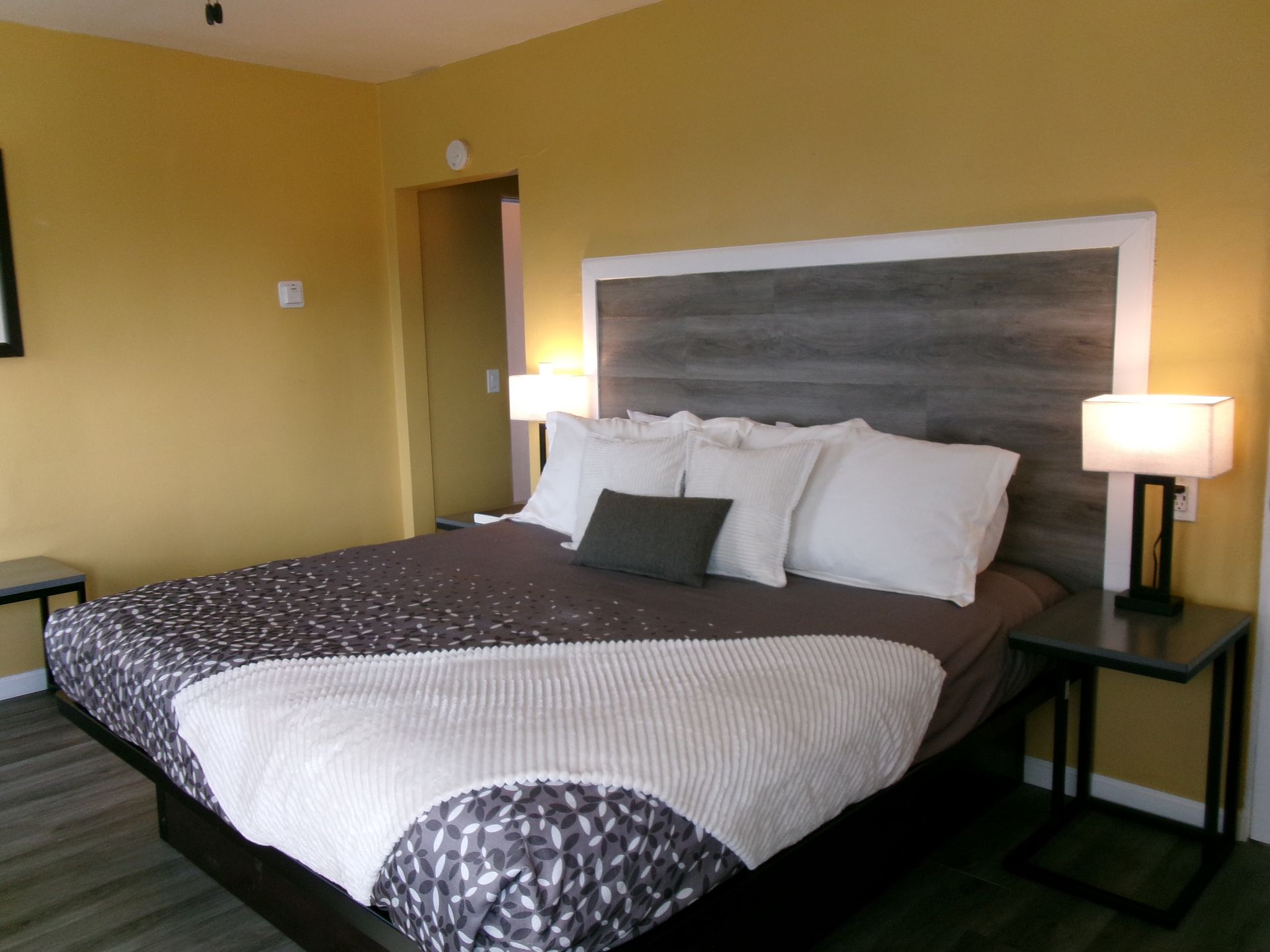 A bedroom featuring a bed with white pillows and a patterned duvet against a wood-paneled headboard and yellow walls.