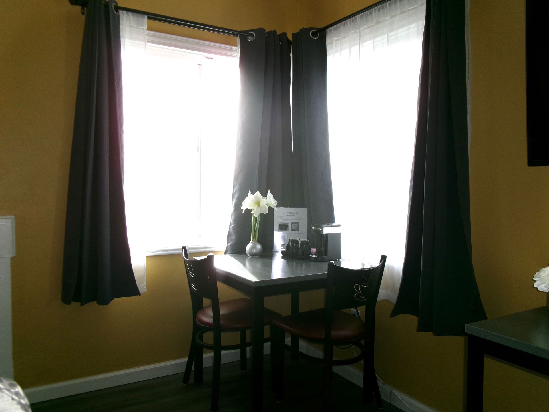 A small table with two chairs sits between two windows draped with dark curtains against gold-painted walls.