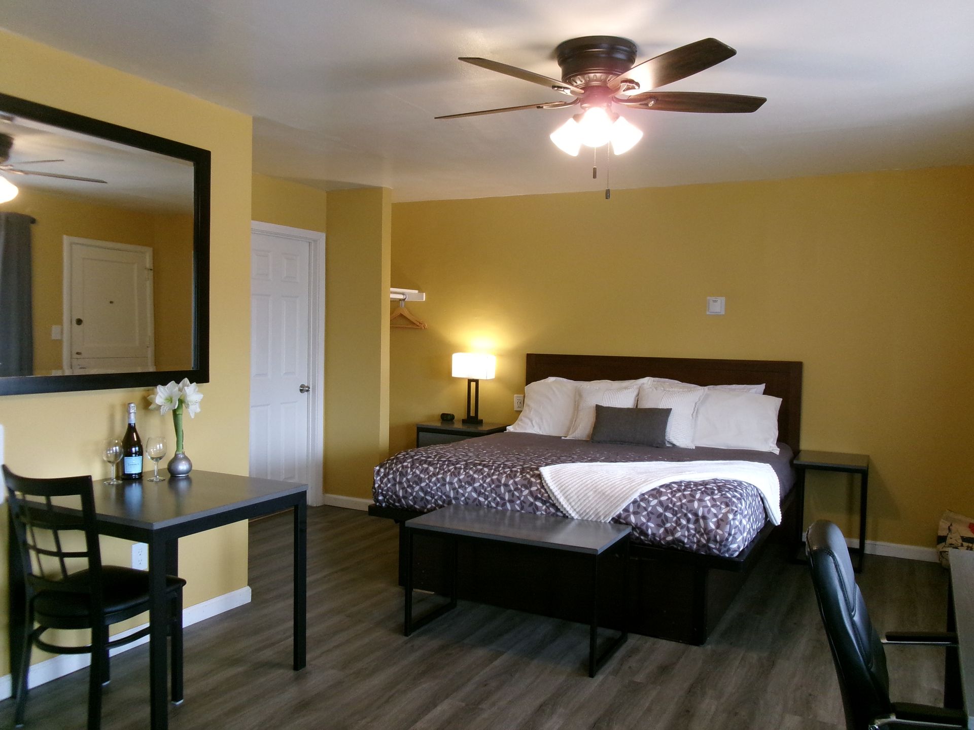 A hotel room with yellow walls, a king bed with white bedding, a desk with a chair, and a large mirror.
