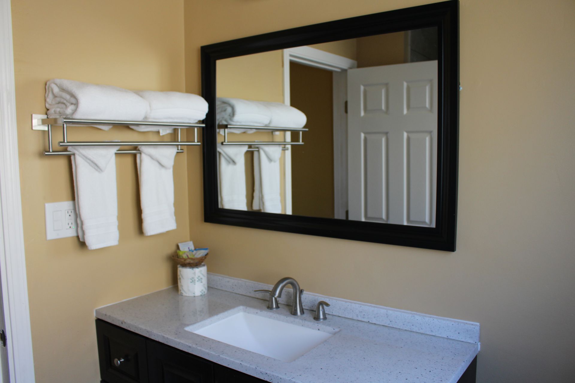 A bathroom vanity with a white countertop, sink, dark cabinets, a mirror reflecting a white door, and hanging white towels.