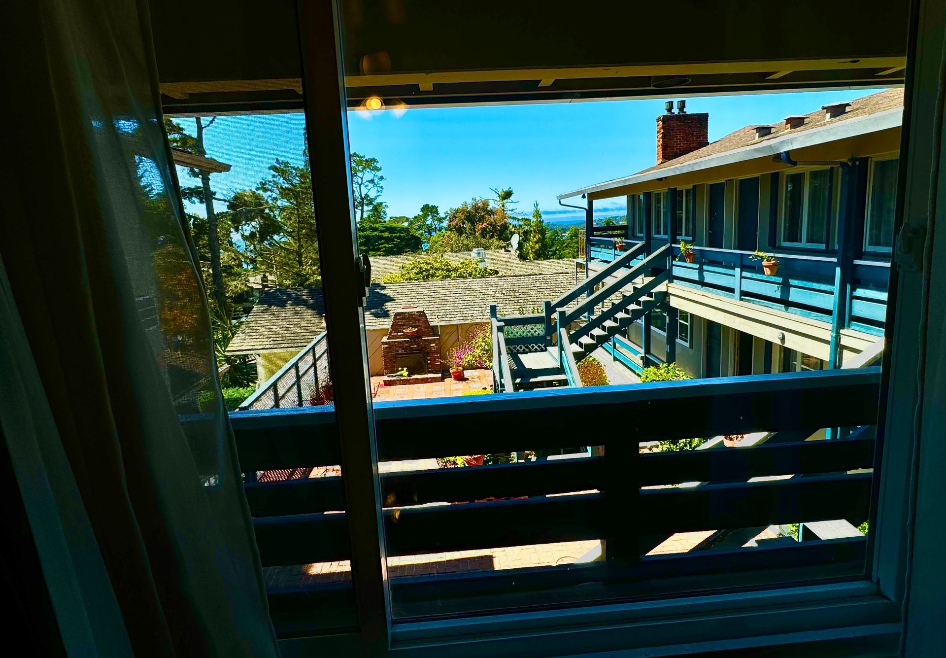 A view from a window showing a two-story blue motel building with exterior stairs and a sunny coastal setting.