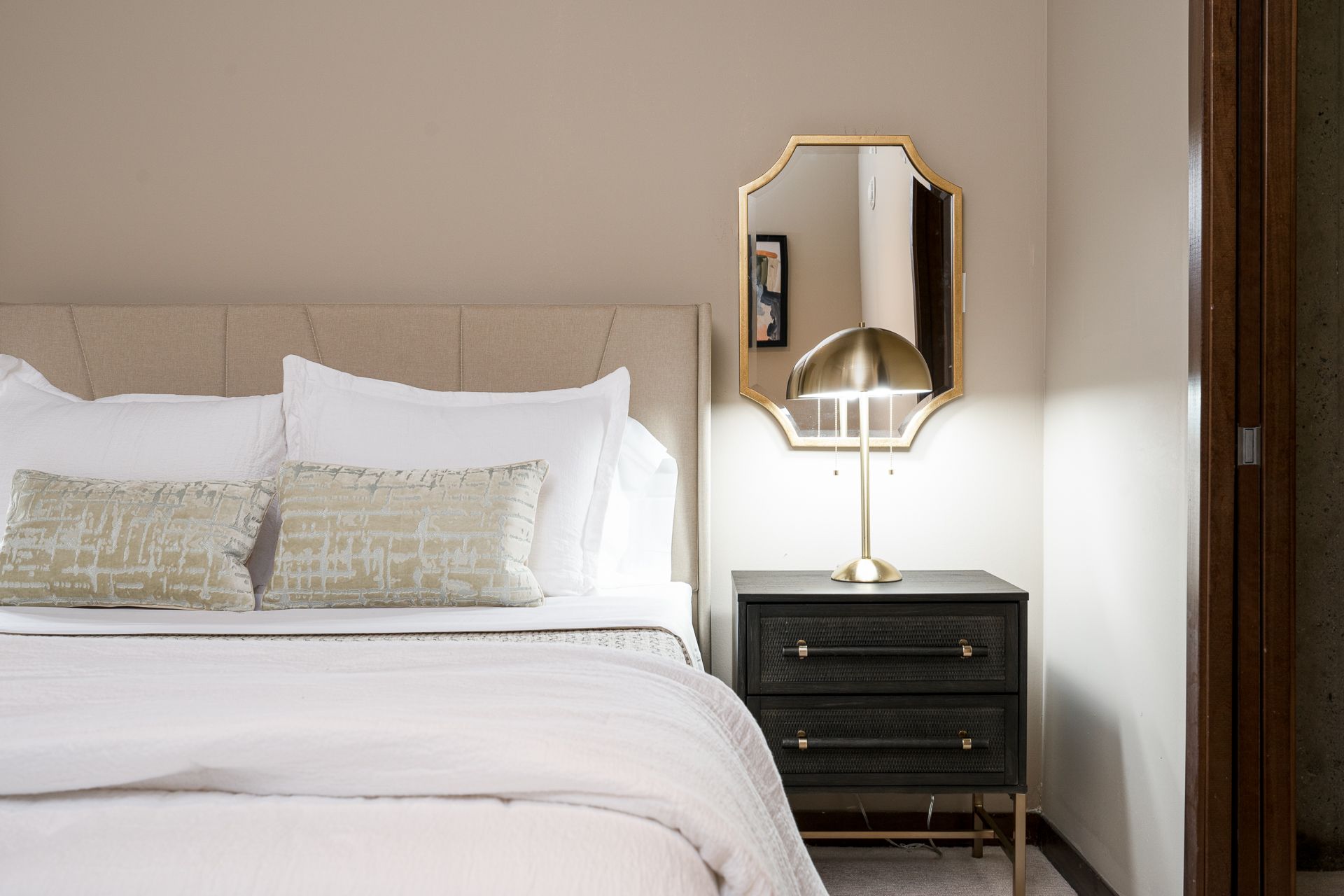A bedroom with a bed , nightstand , mirror and lamp.