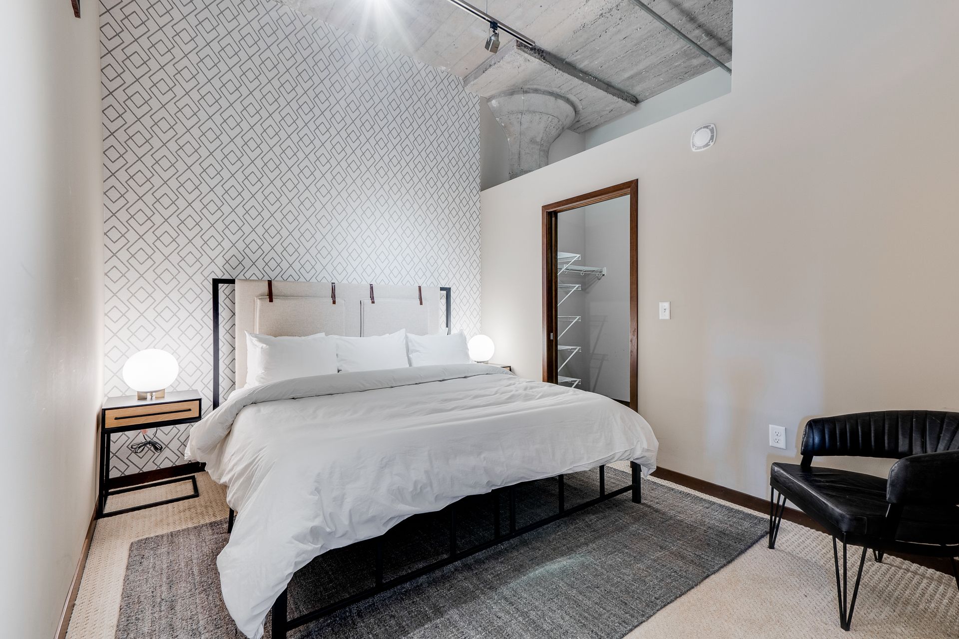 A bedroom with a bed , chair , nightstand and rug.