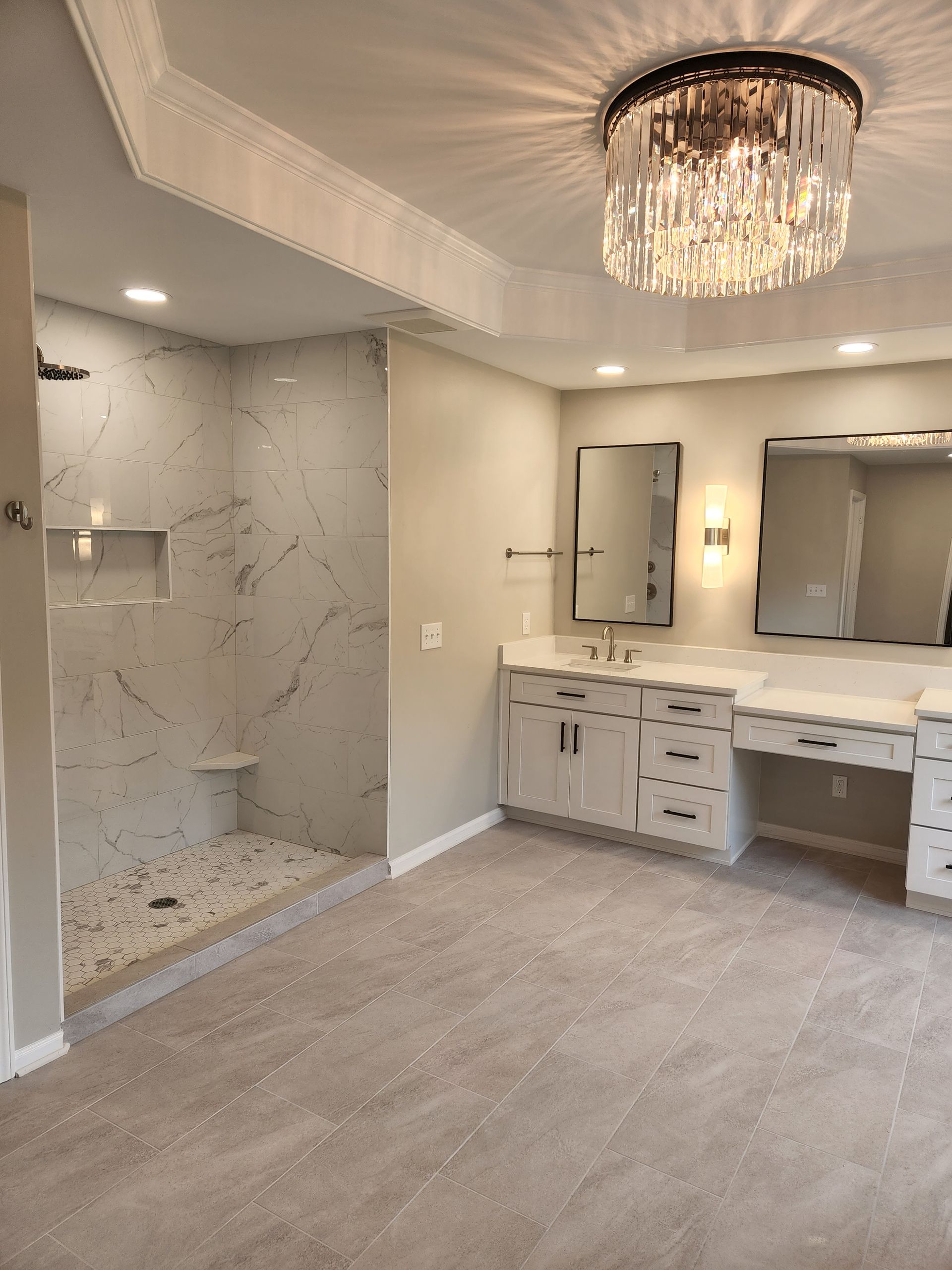 A bathroom with a walk in shower , sinks , mirrors and a chandelier.