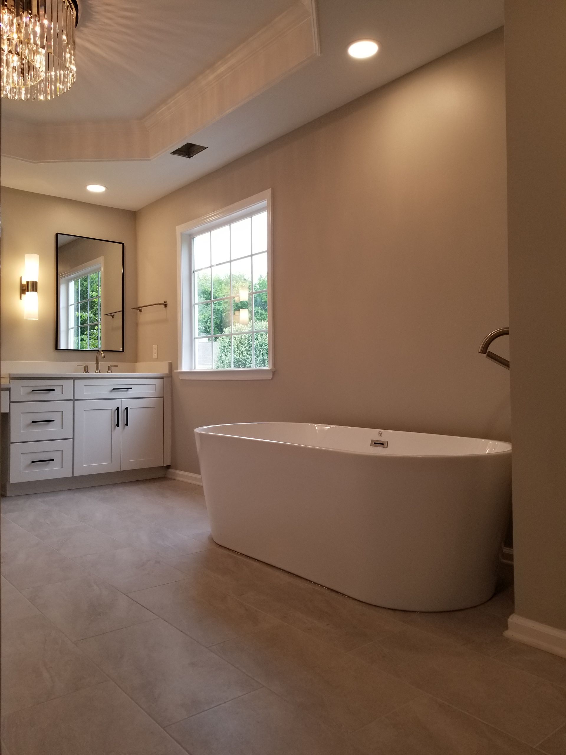 A bathroom with a tub, sink, mirror and window.