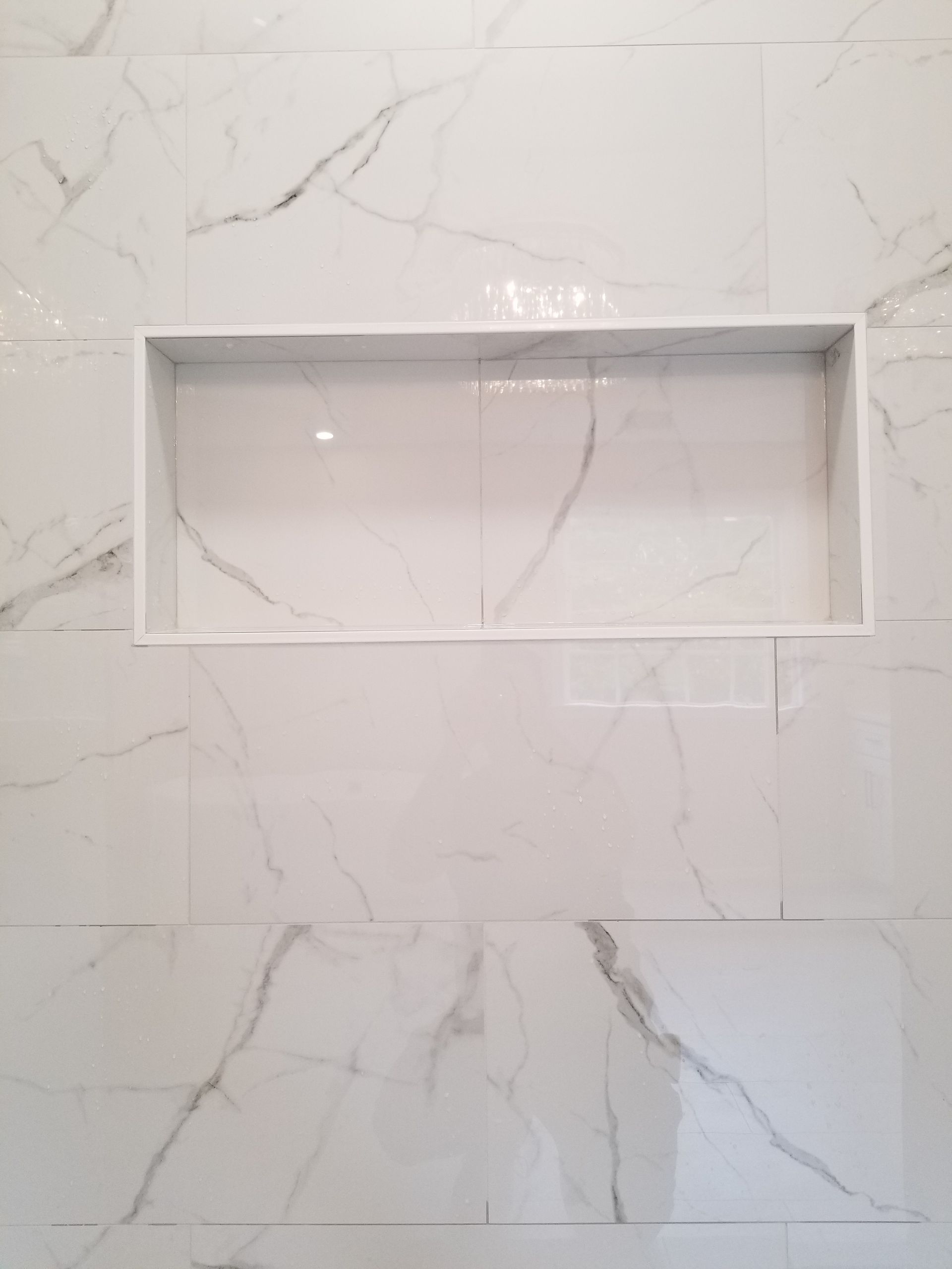 A shower niche is built into a white marble wall.