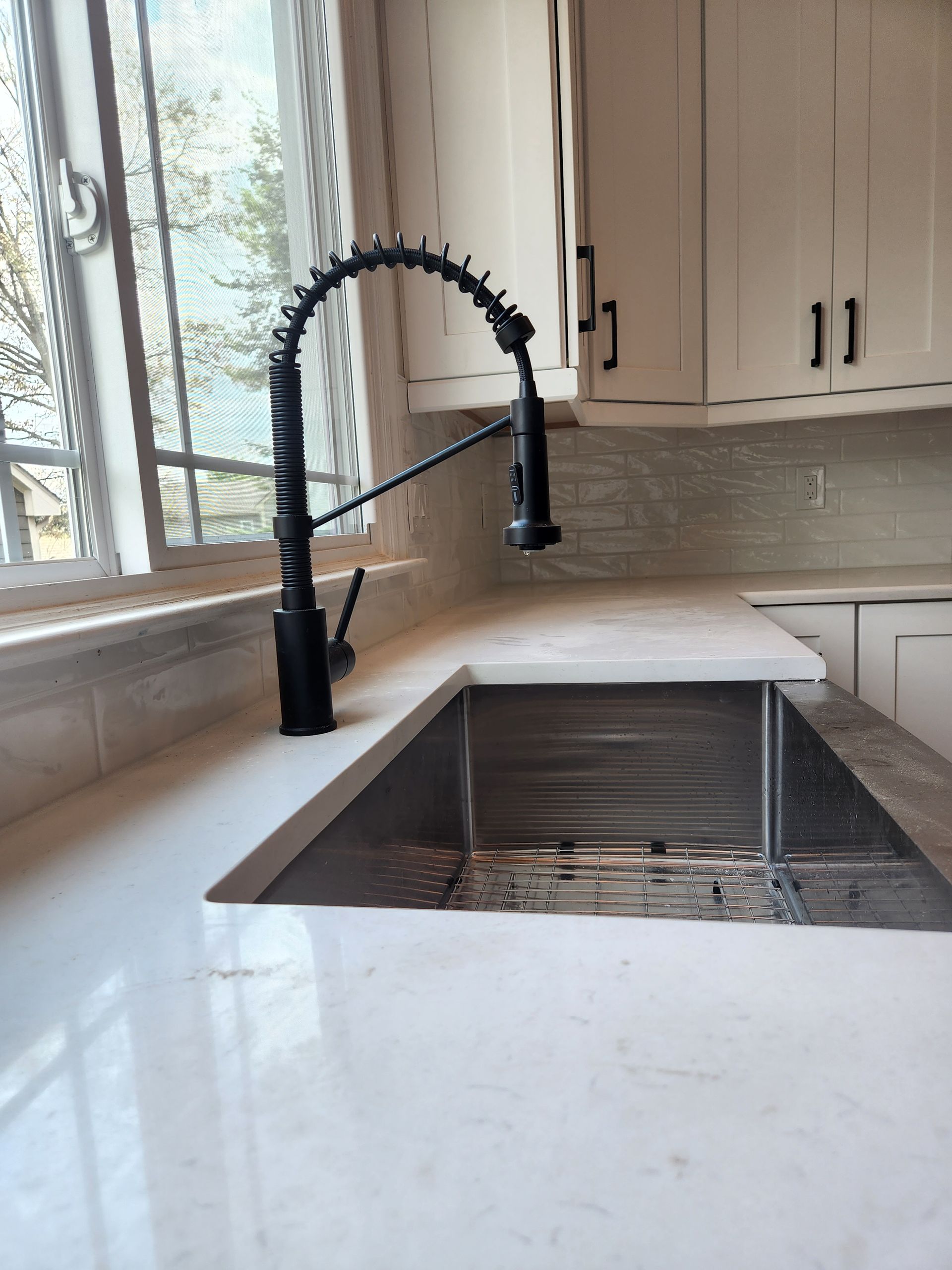 A kitchen sink with a black faucet and white counter tops