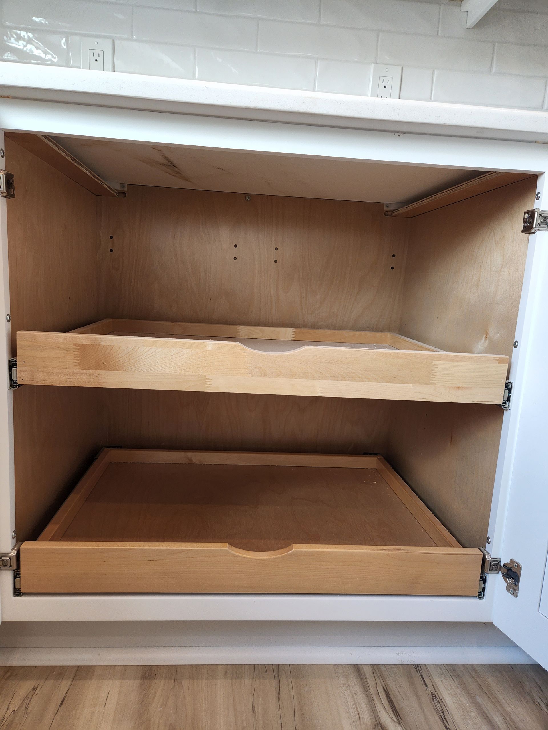 A kitchen cabinet with two wooden drawers pulled out of it.