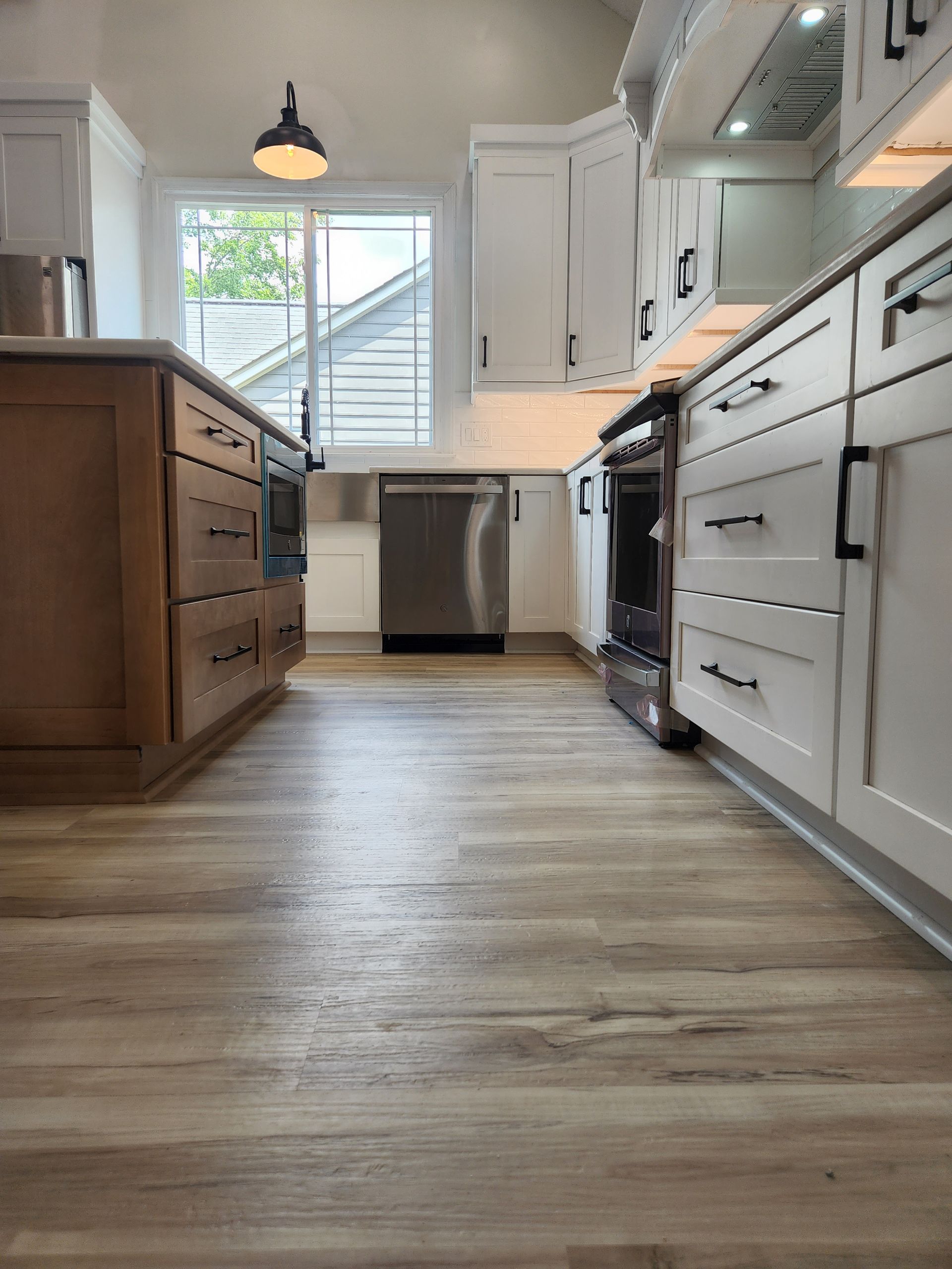 A kitchen with wooden floors , white cabinets, and stainless steel appliances.