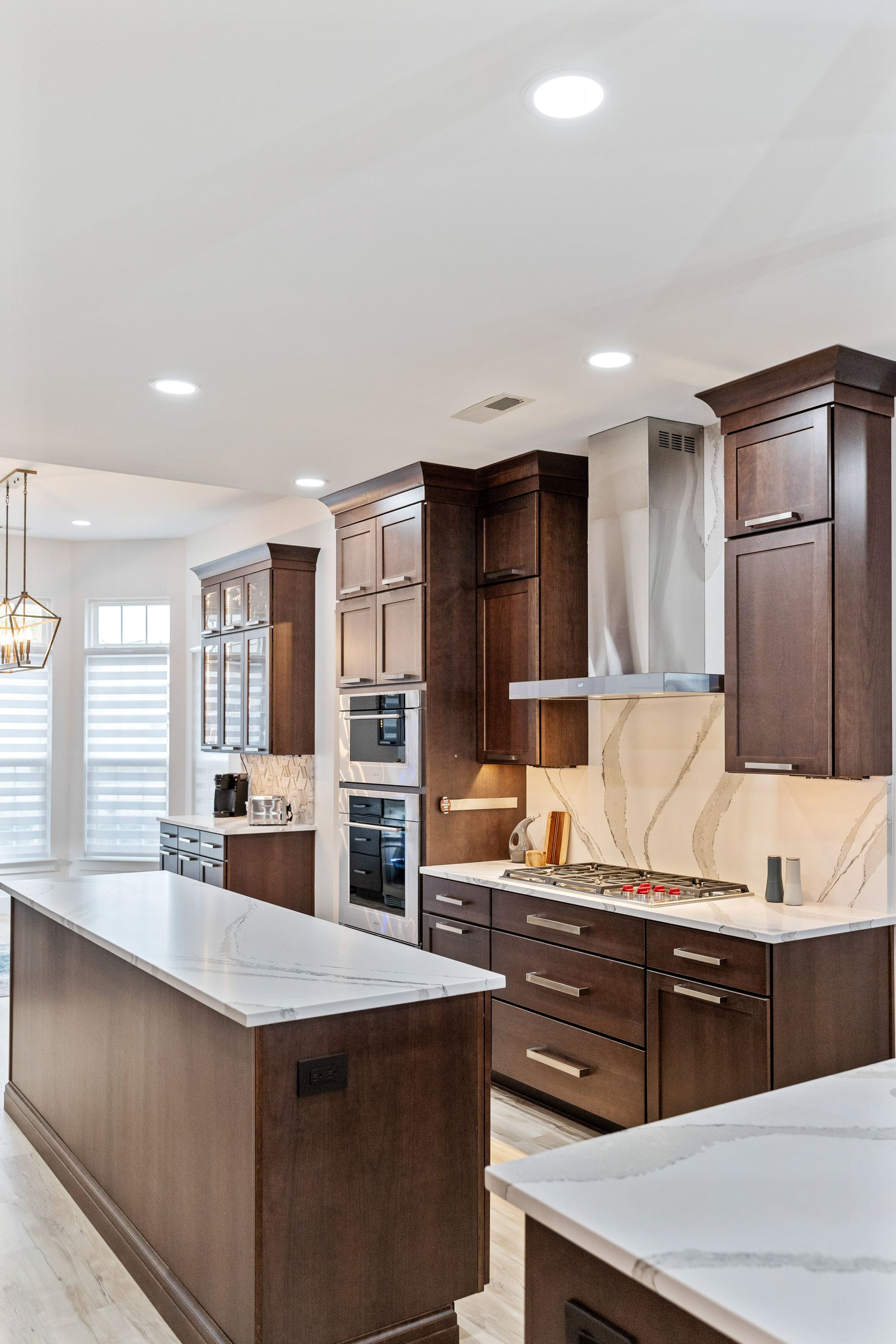 A kitchen with wooden cabinets , white counter tops , stainless steel appliances and a large island.