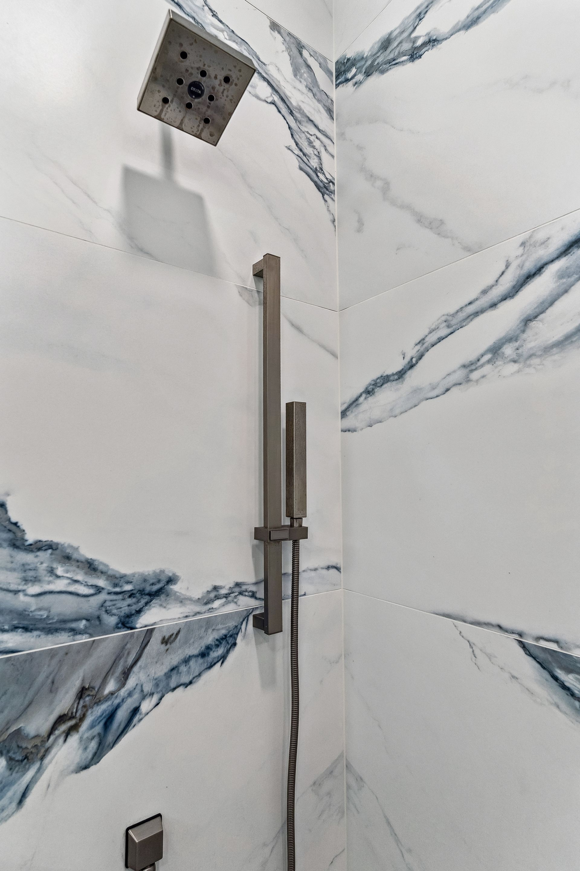 A close up of a shower head in a bathroom with marble walls.