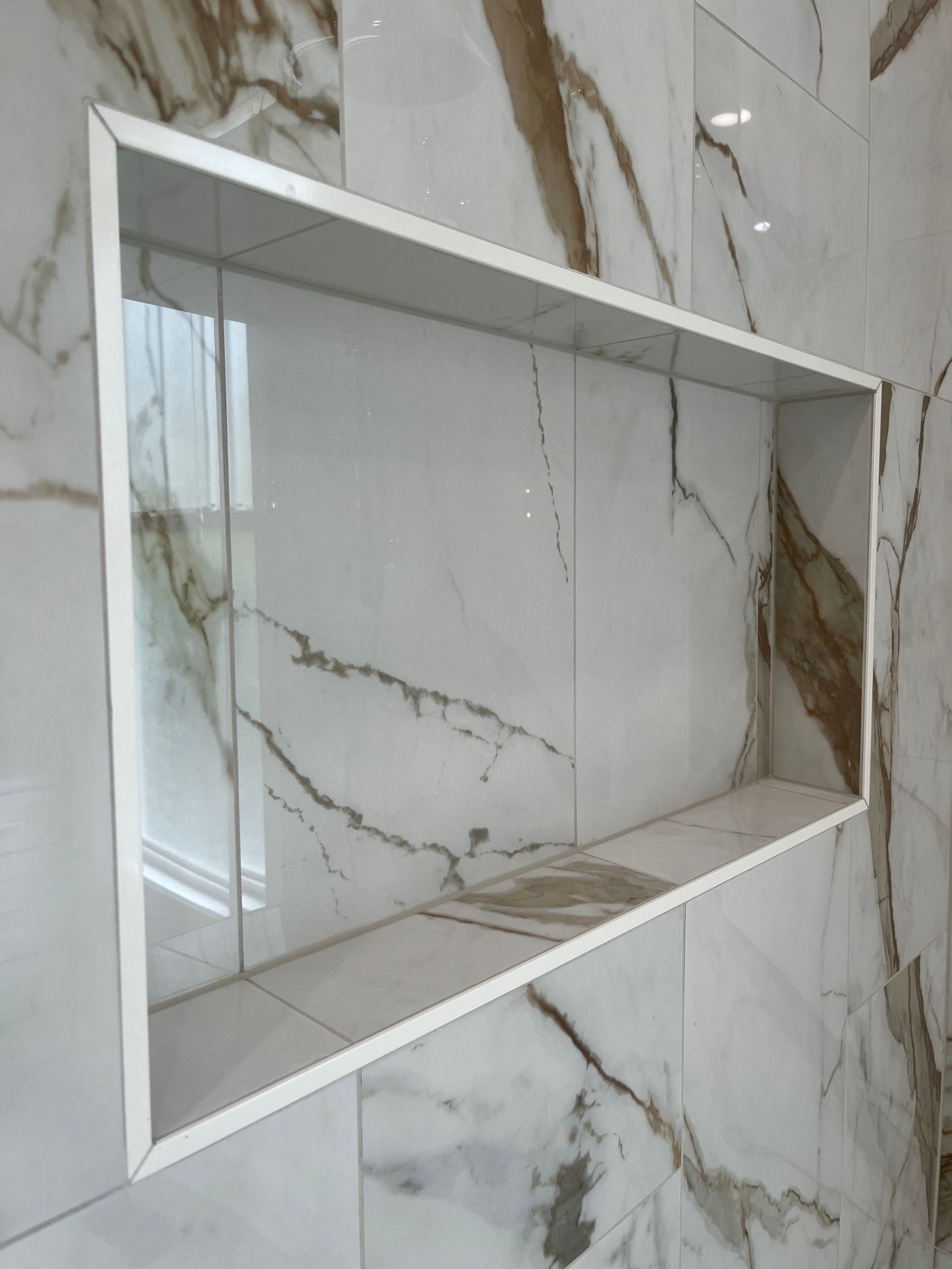 A bathroom with a marble wall and a shelf in the wall.