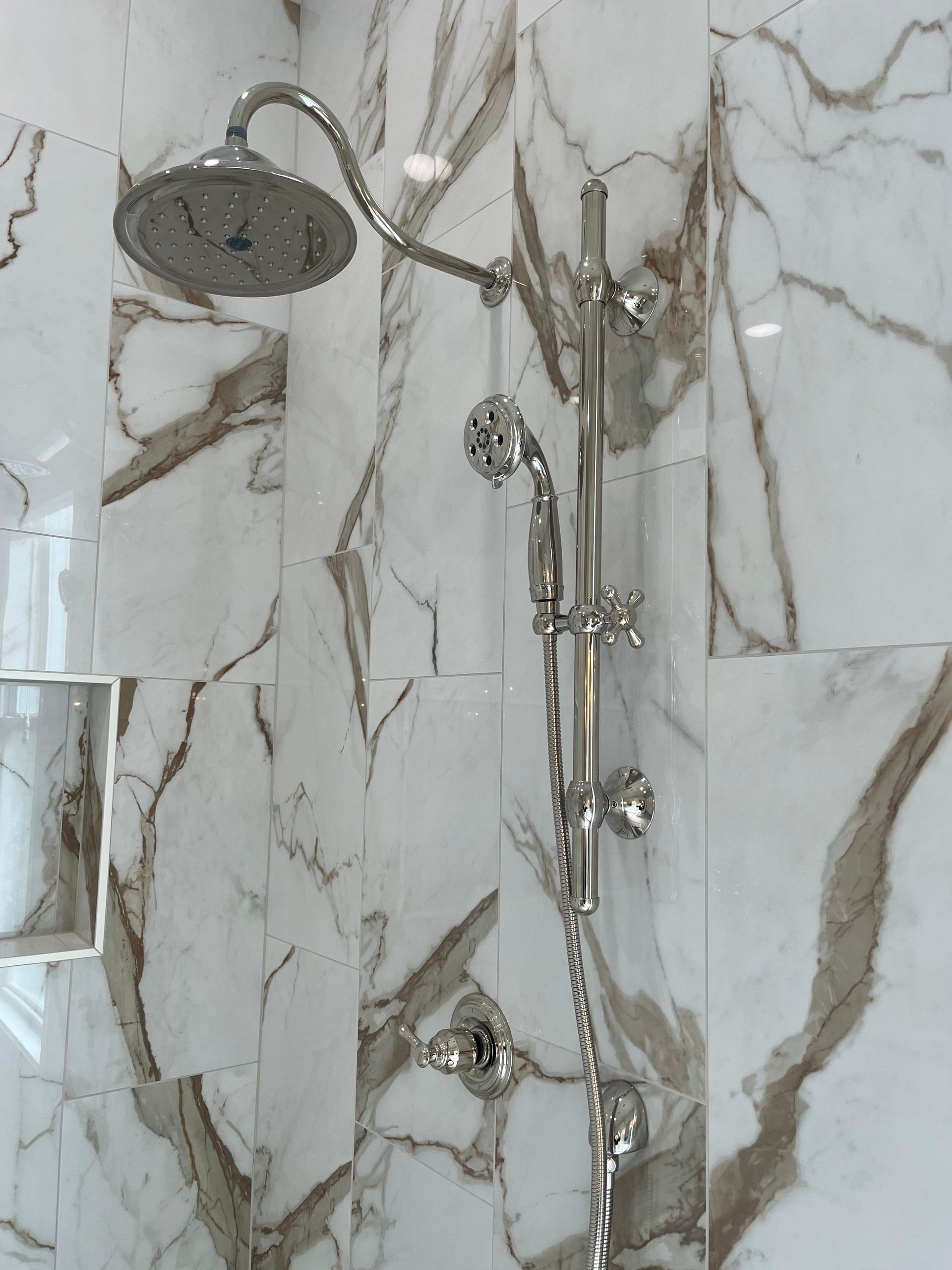 A shower head in a bathroom with marble tiles
