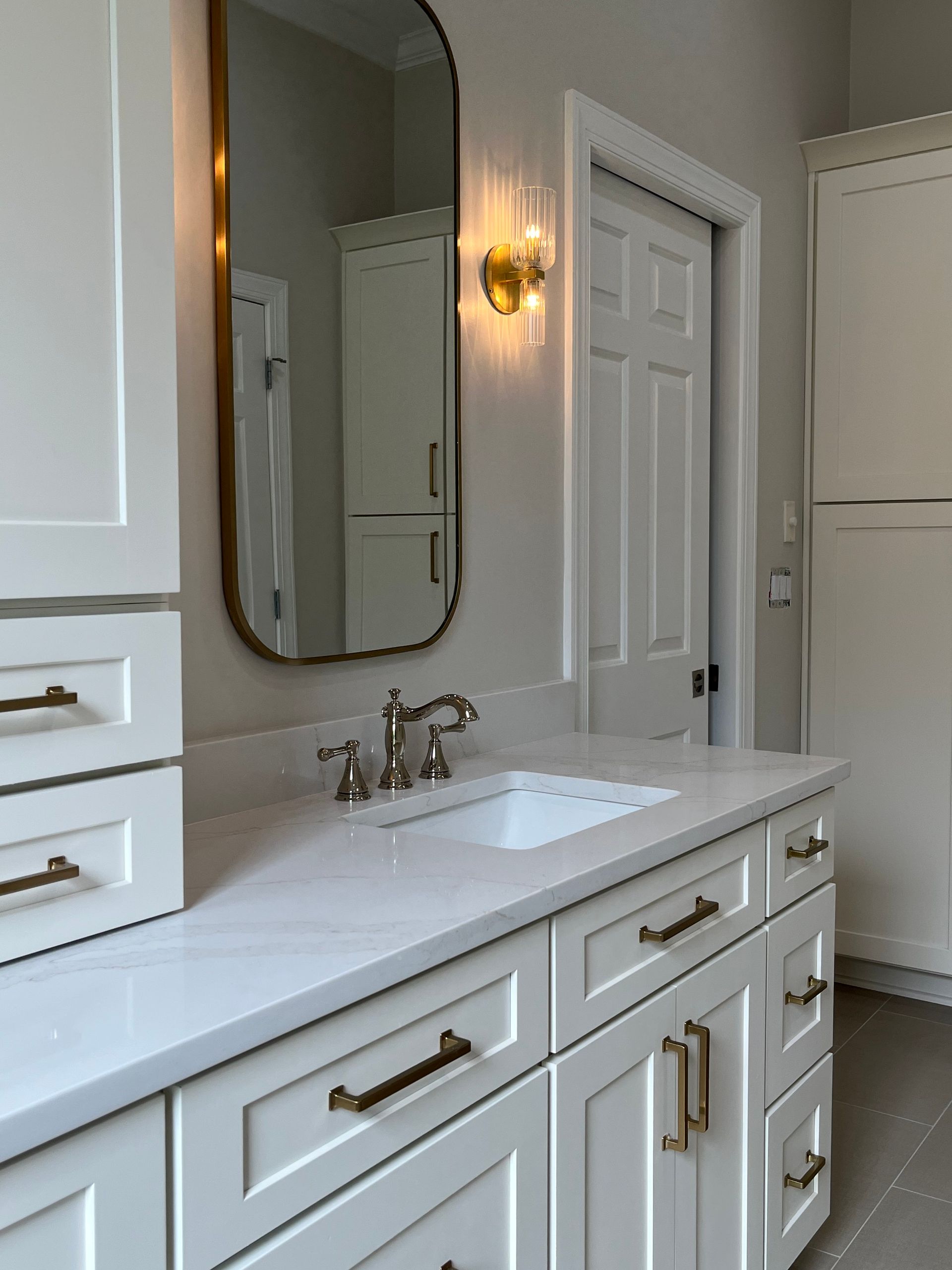 A bathroom with white cabinets a sink and a mirror