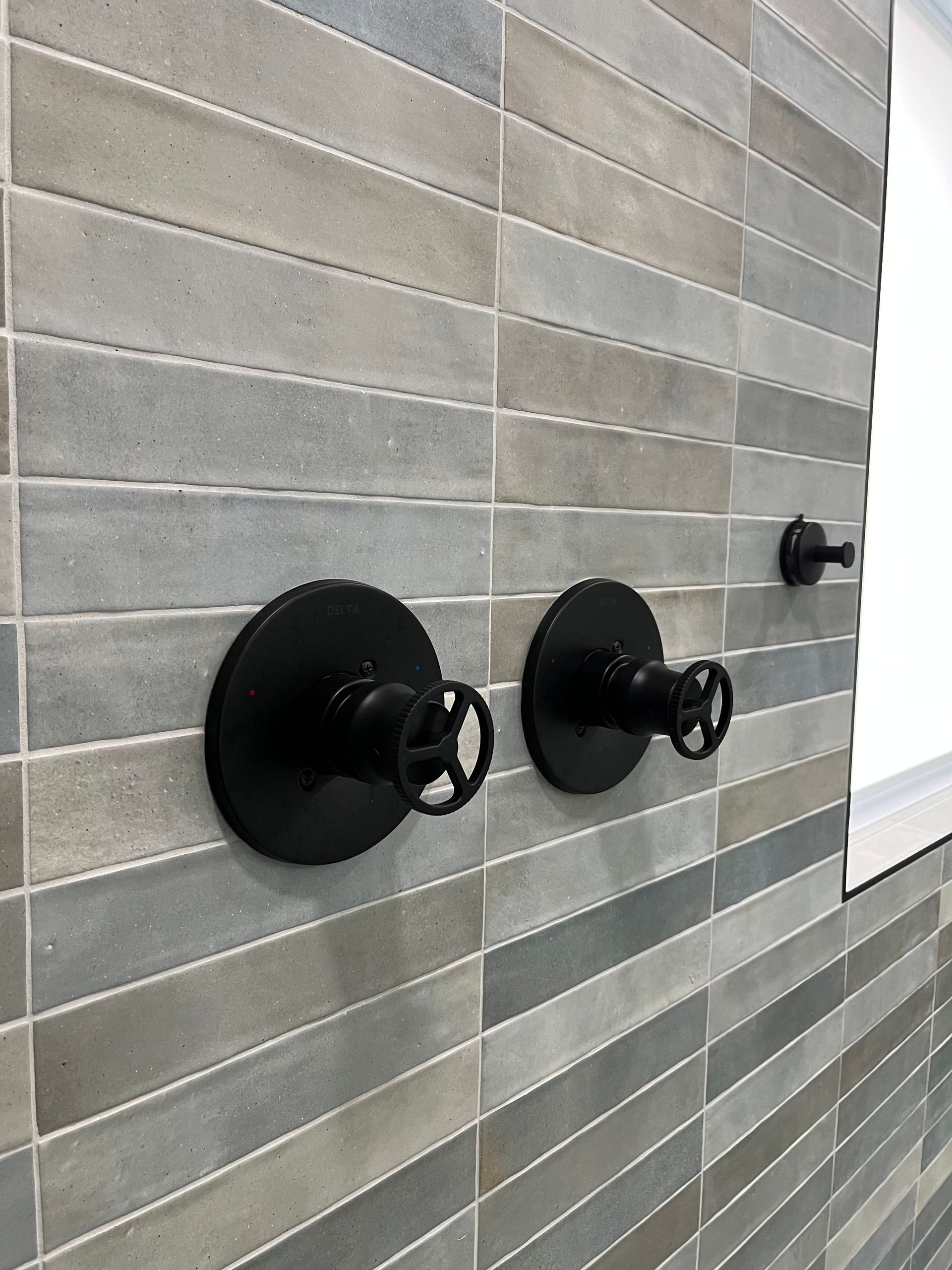 Two black knobs on a tiled wall.