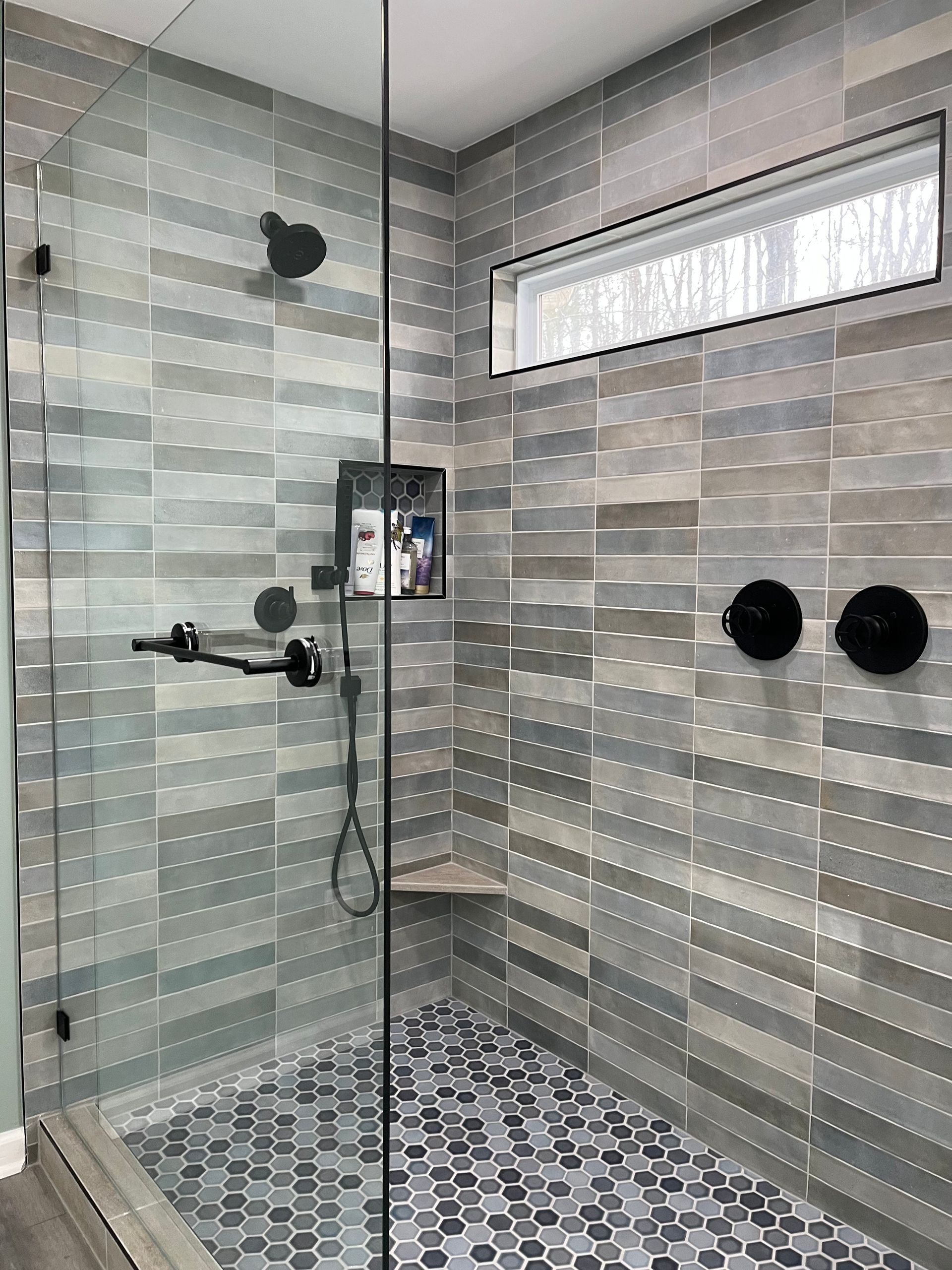A walk in shower with a glass door and a window.