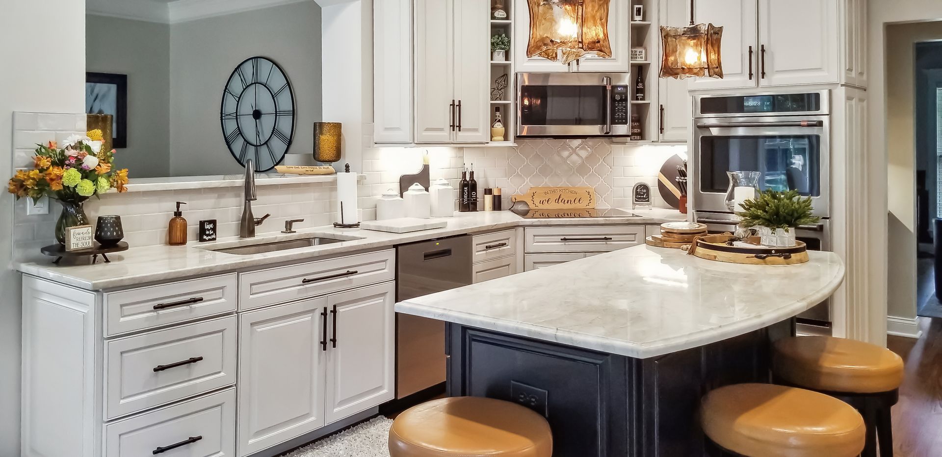 A kitchen with white cabinets , stainless steel appliances , a large island and stools.