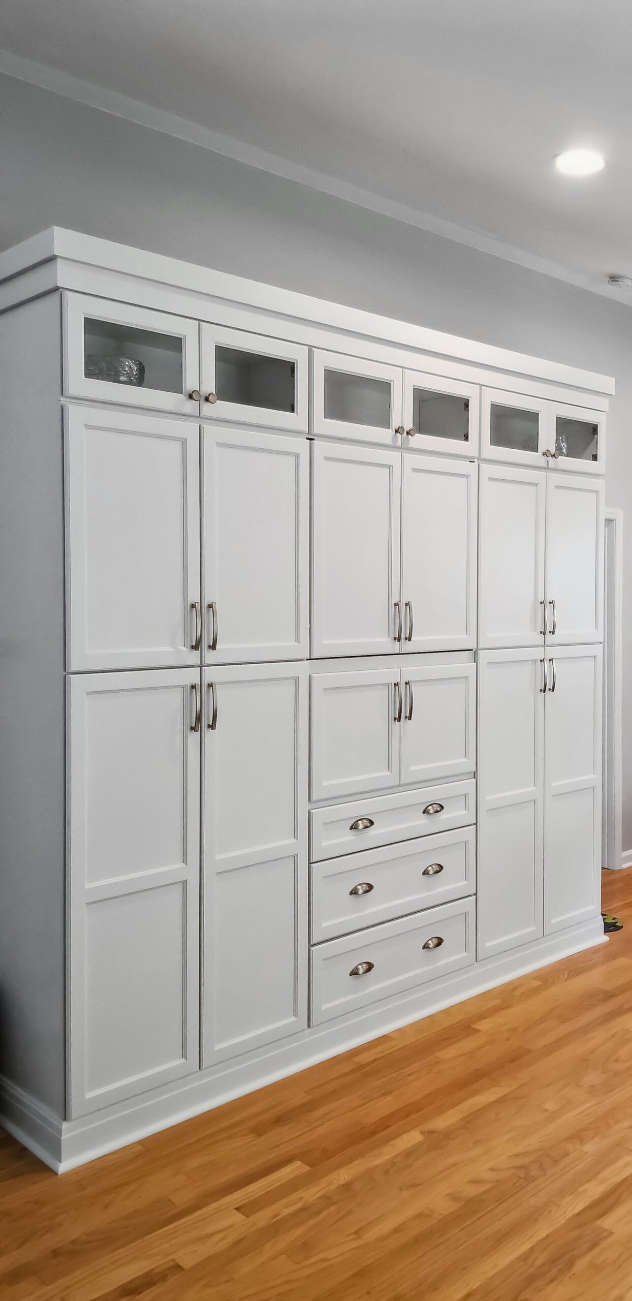 A large white cabinet with glass doors and drawers in a room with hardwood floors.