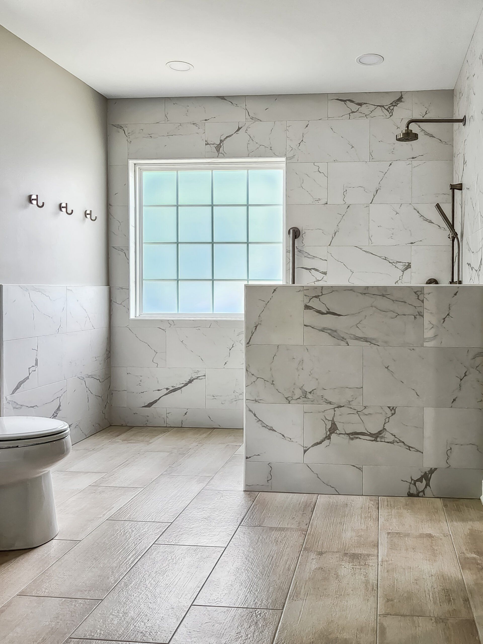 A bathroom with marble tiles, a toilet and a window.
