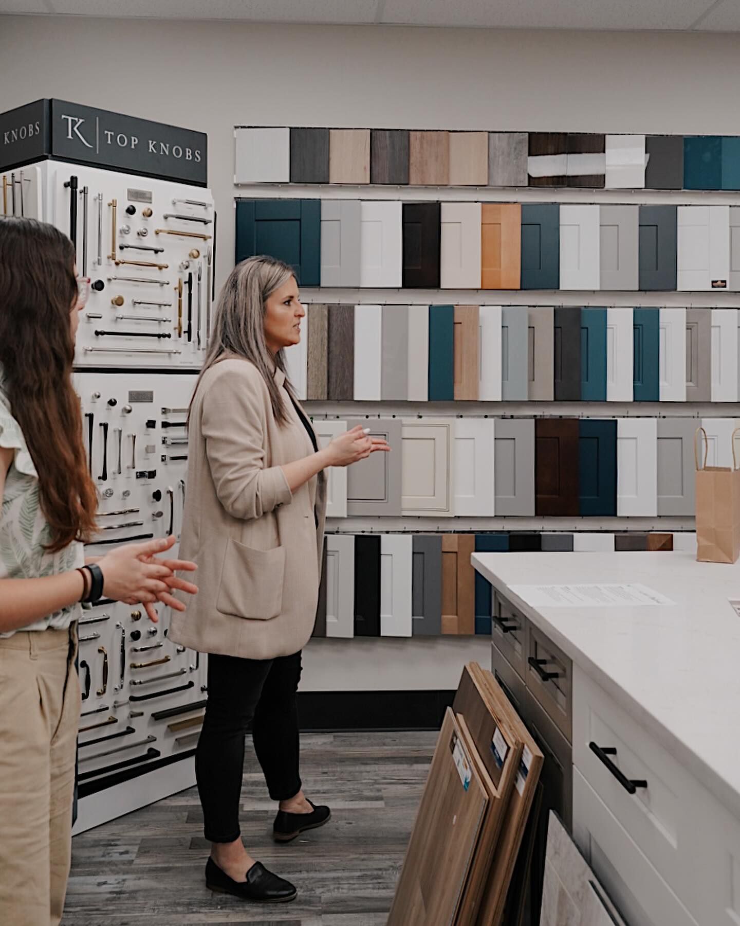 Two women are standing in a kitchen showroom looking at cabinets.