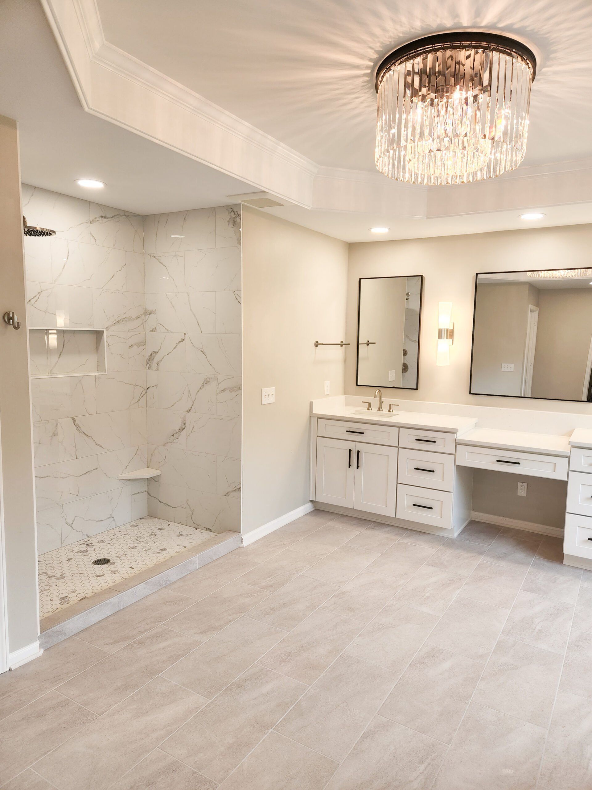 A bathroom with a walk in shower, sink, mirror and chandelier.
