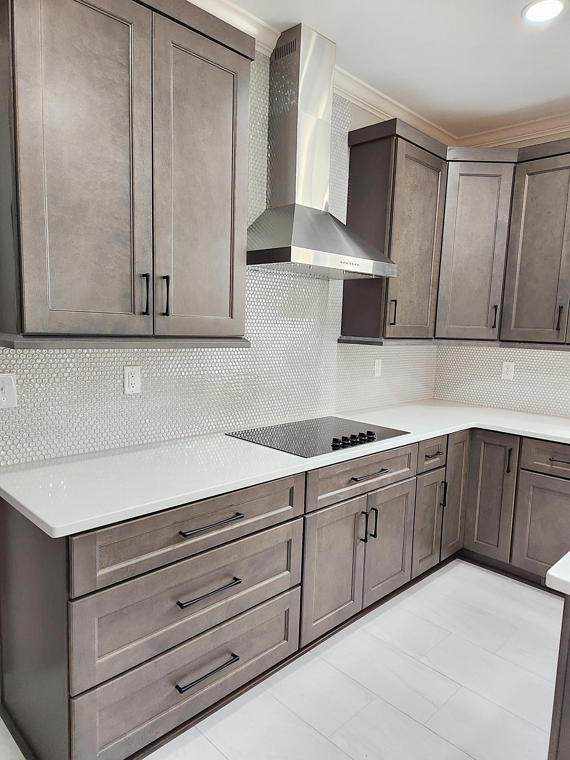 A kitchen with gray cabinets and white counter tops and a stove top oven.