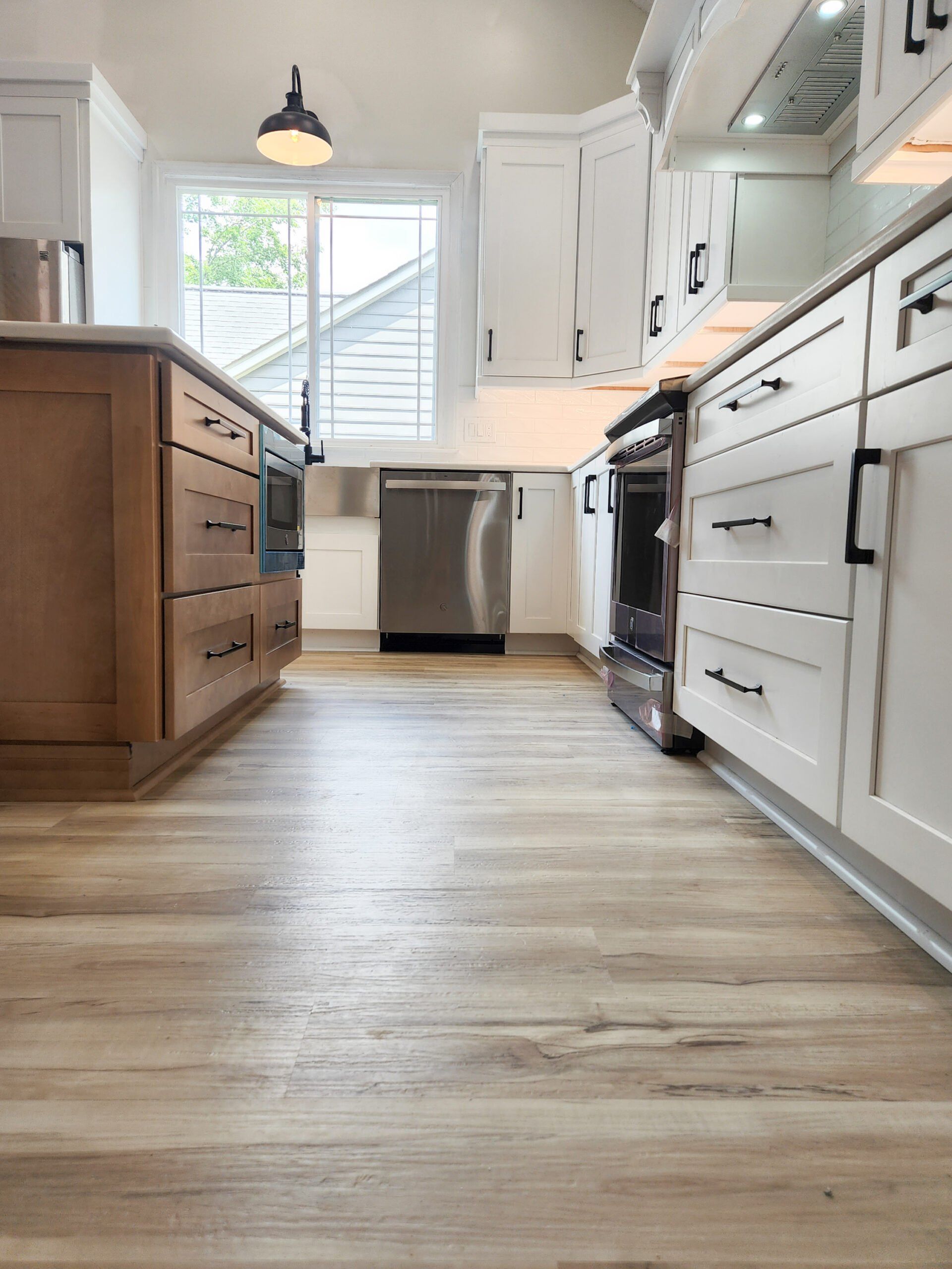 A kitchen with wooden floors , white cabinets and stainless steel appliances.