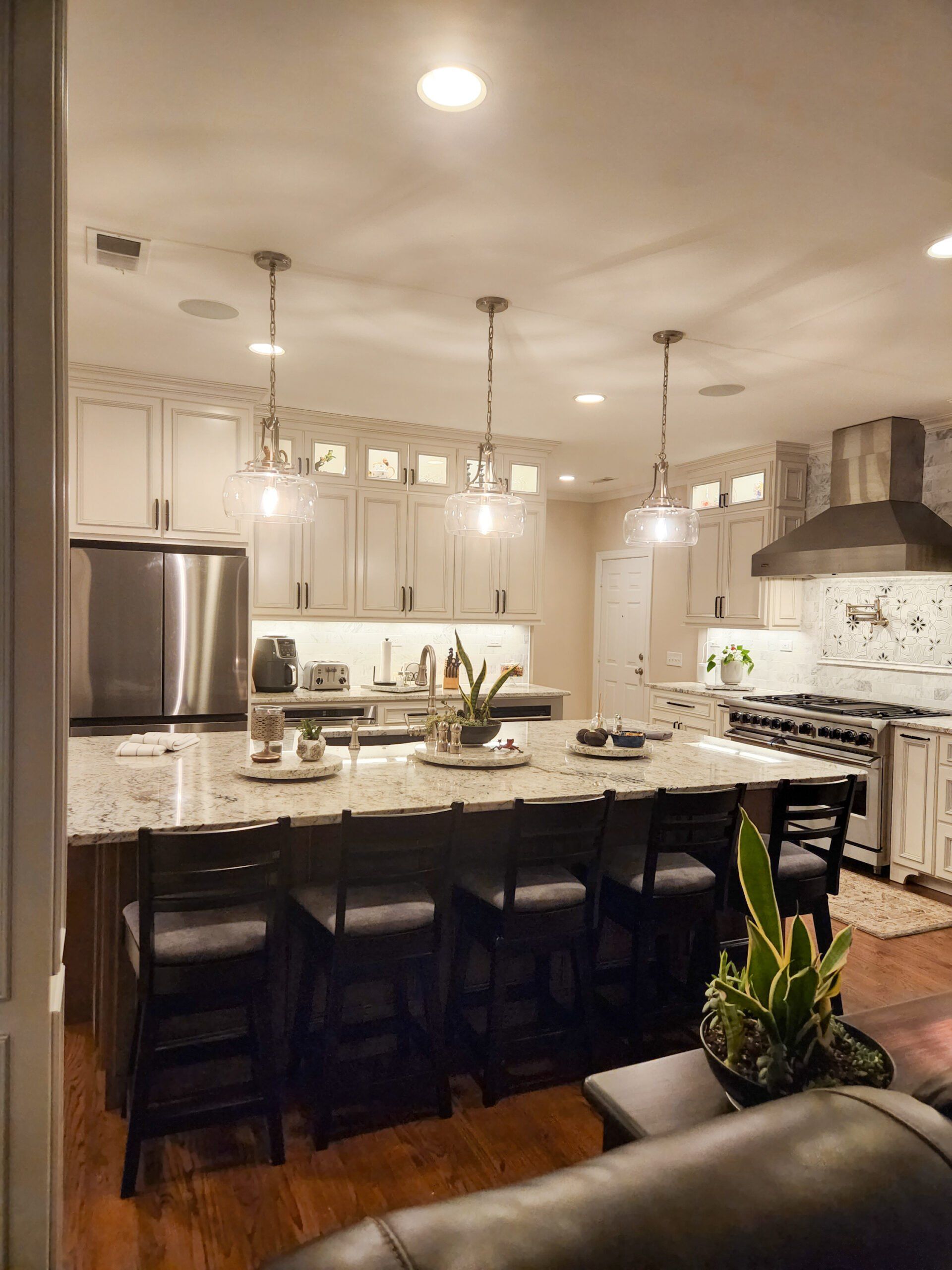 A kitchen with white cabinets , stainless steel appliances , a large island and a couch.