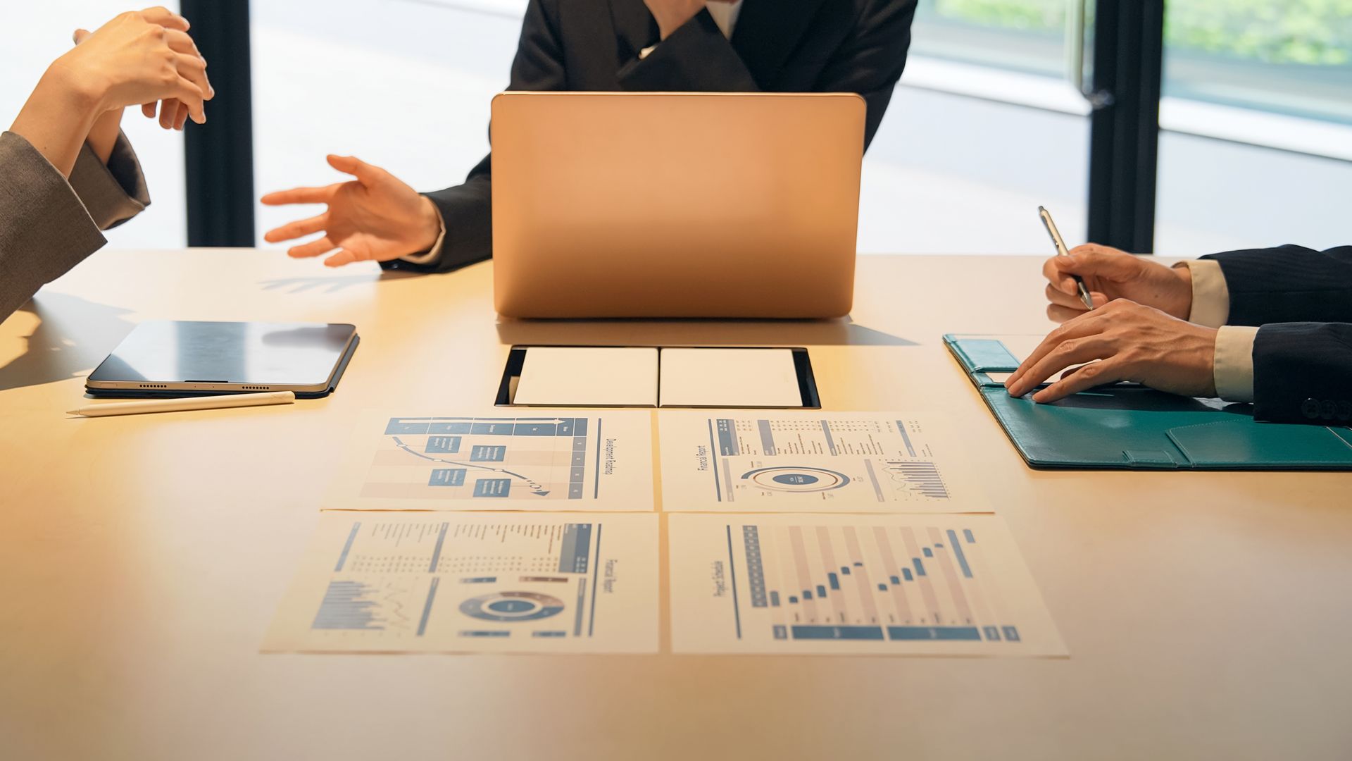 Business meeting with laptop, charts, and hands gesturing around a conference table.