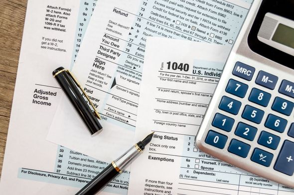 Tax forms, calculator, and pens on a wooden surface, indicating tax preparation.