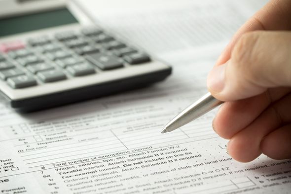 Hand holding pen over tax form, calculator in background.