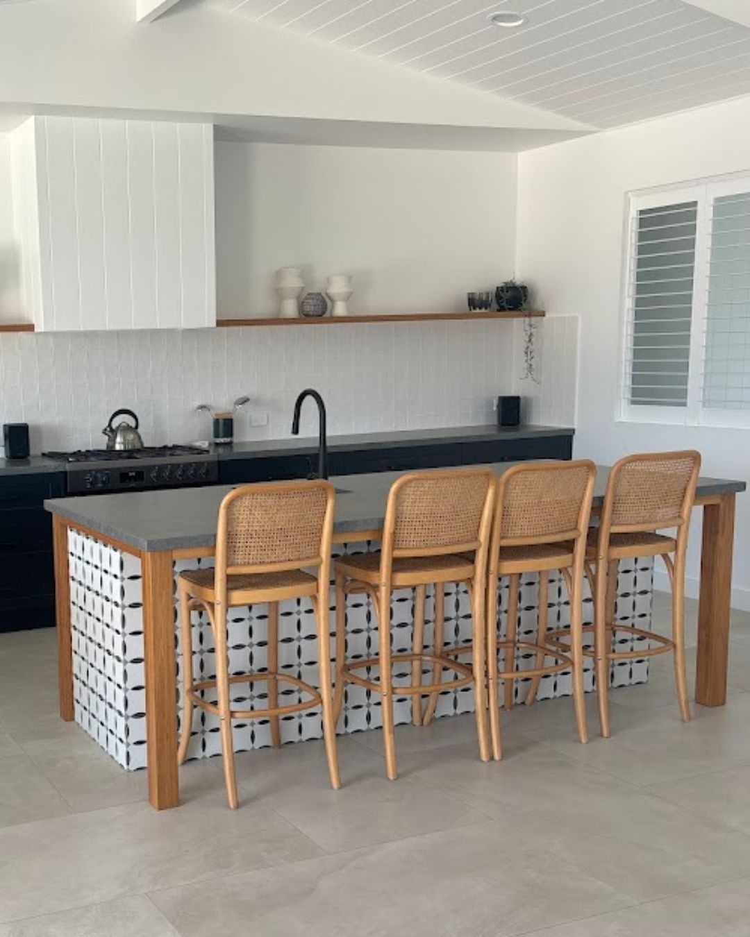 Modern kitchen with island, black countertop, wicker bar stools, and light wood cabinetry.