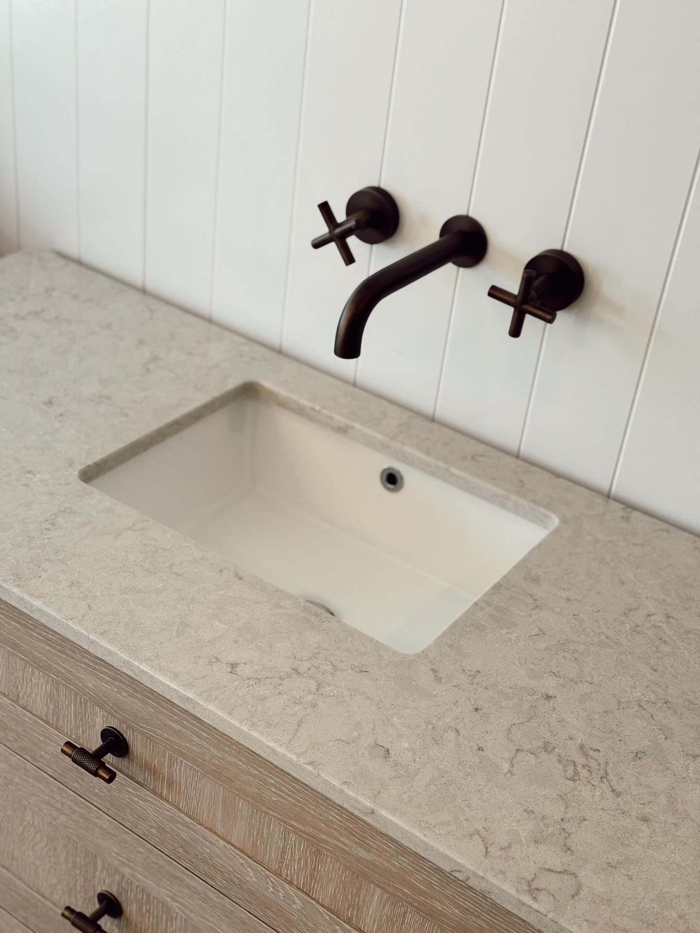 Modern bathroom sink with beige countertop and black wall-mounted faucet against white tile backsplash