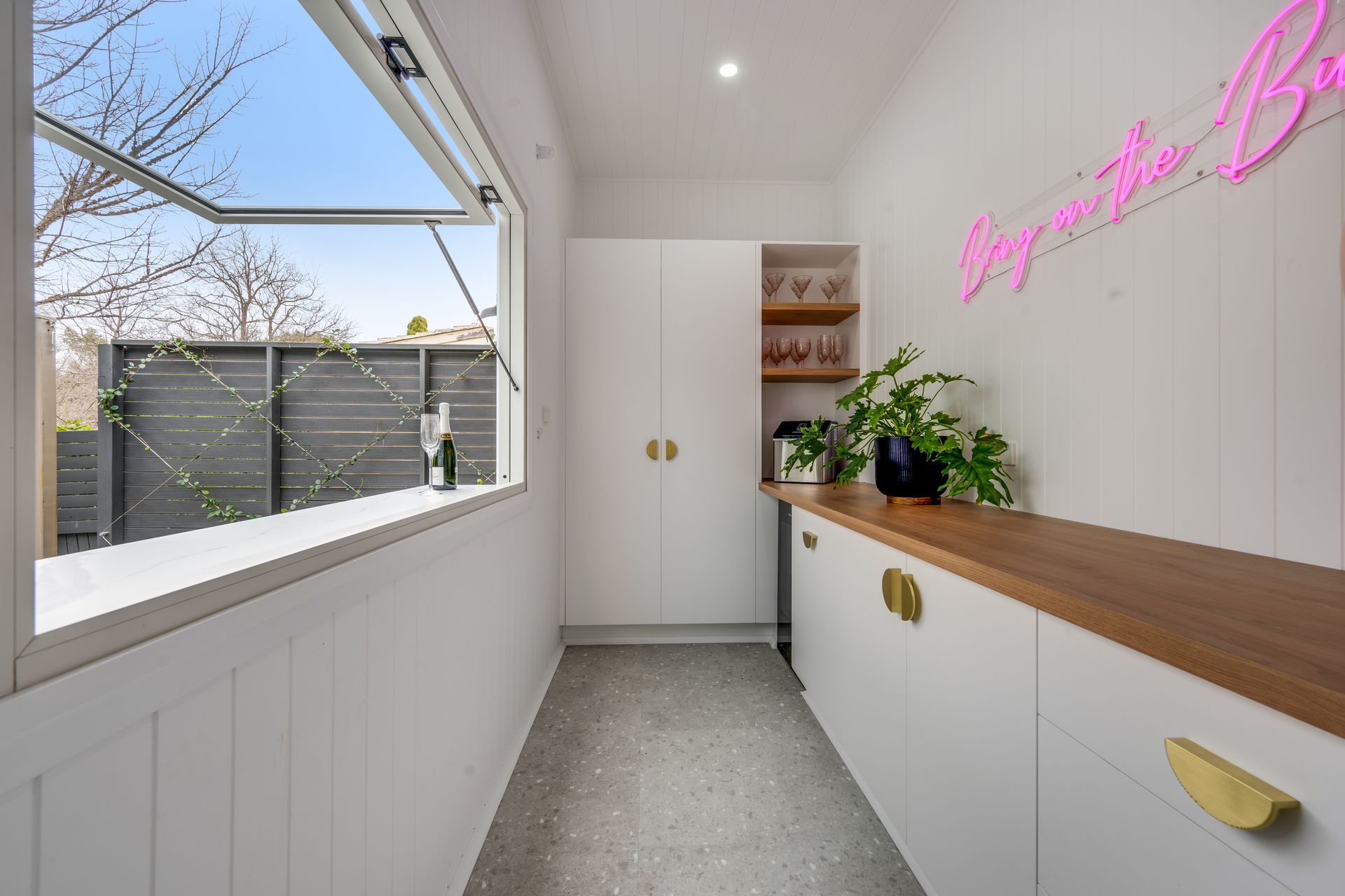 Bright modern hallway with white cabinetry, wood countertop, plants, and pink neon wall sign