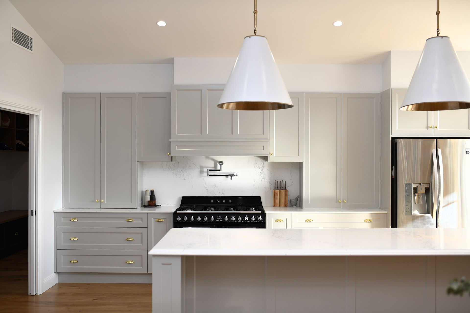 Modern white kitchen with gray cabinets, marble island, pendant lights, and stainless steel appliances