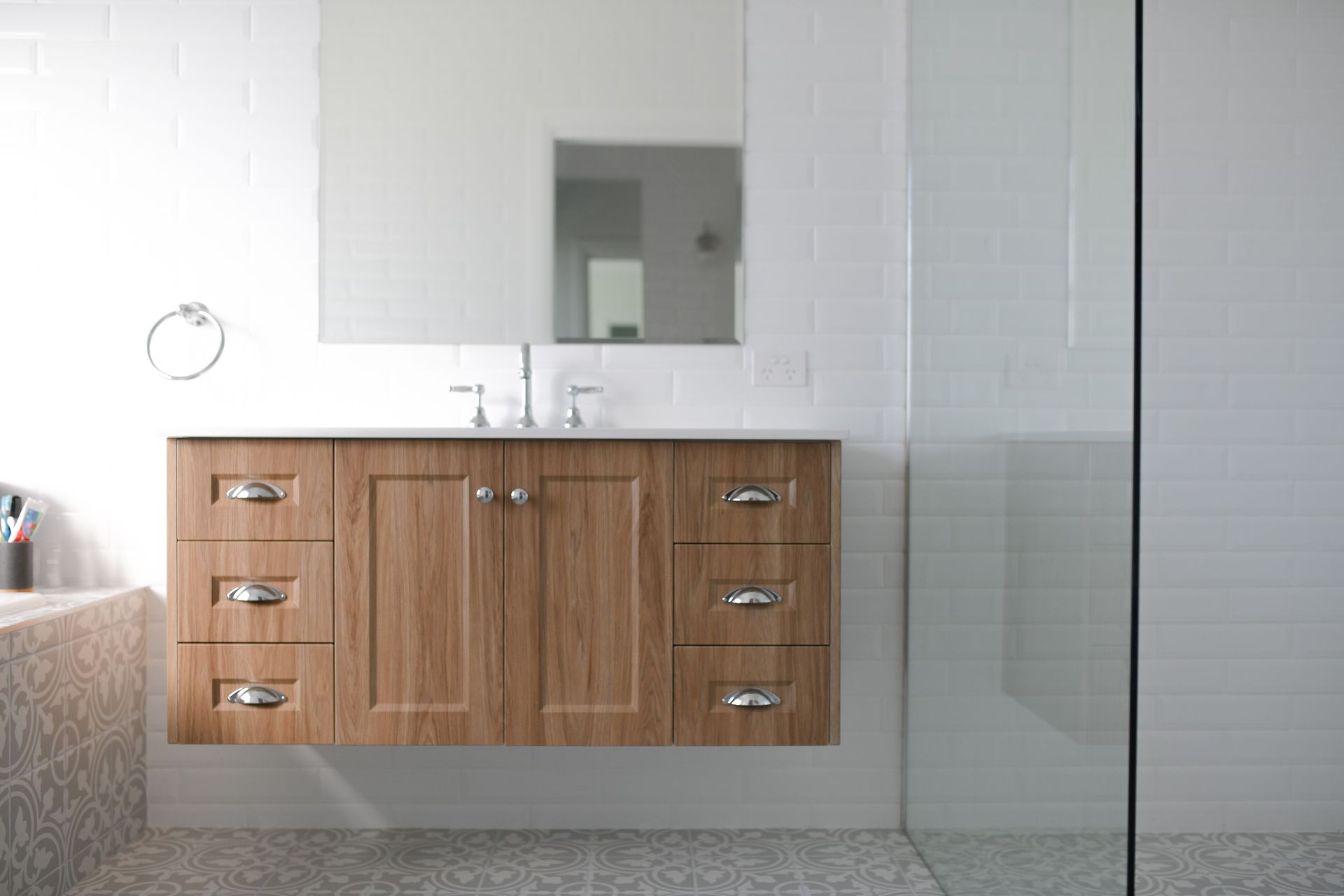 Modern bathroom vanity with wood cabinets, white countertop, mirror, and glass shower enclosure