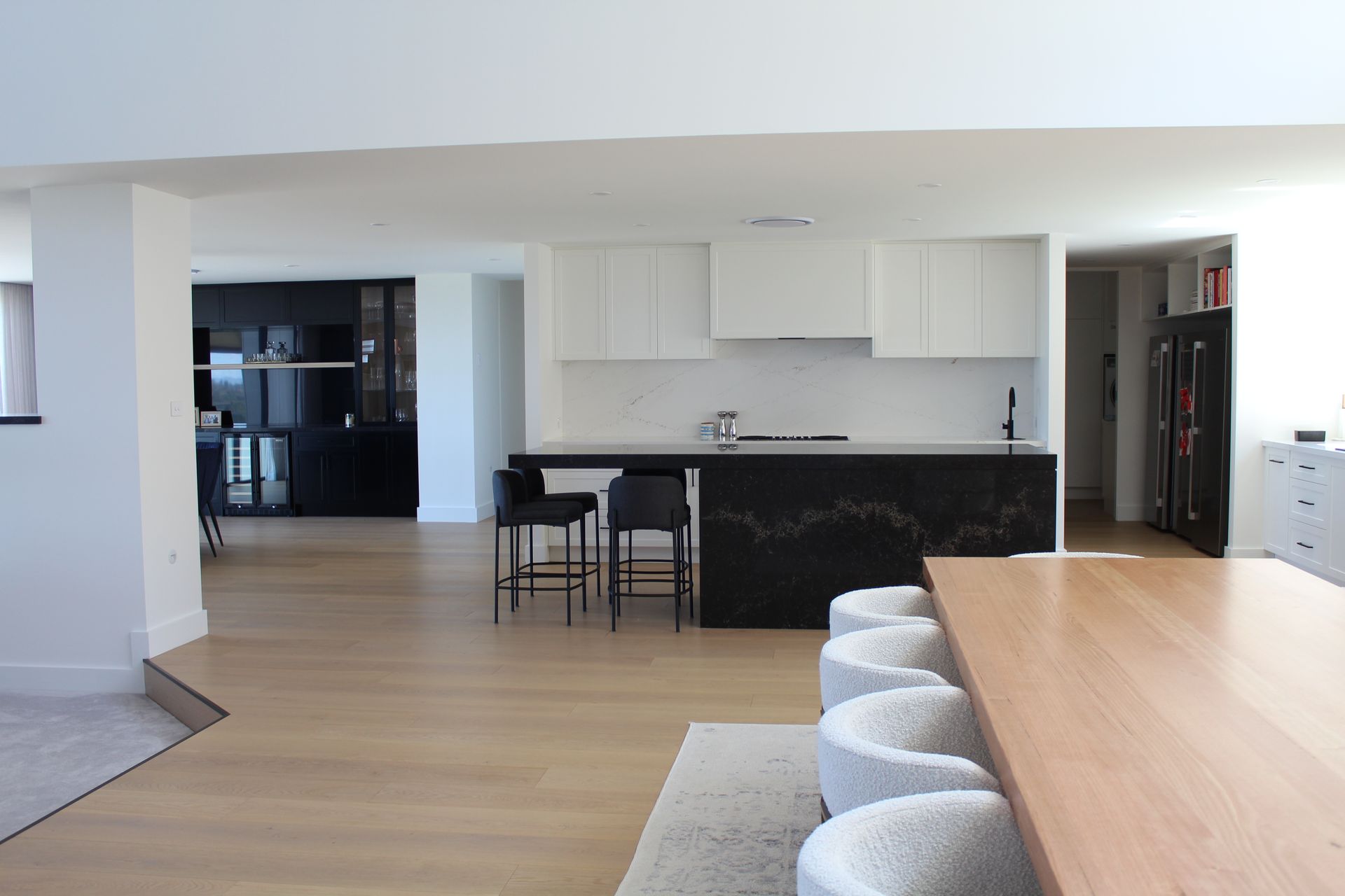 Modern open-plan kitchen and dining area with white walls, wood floors, and black bar stools