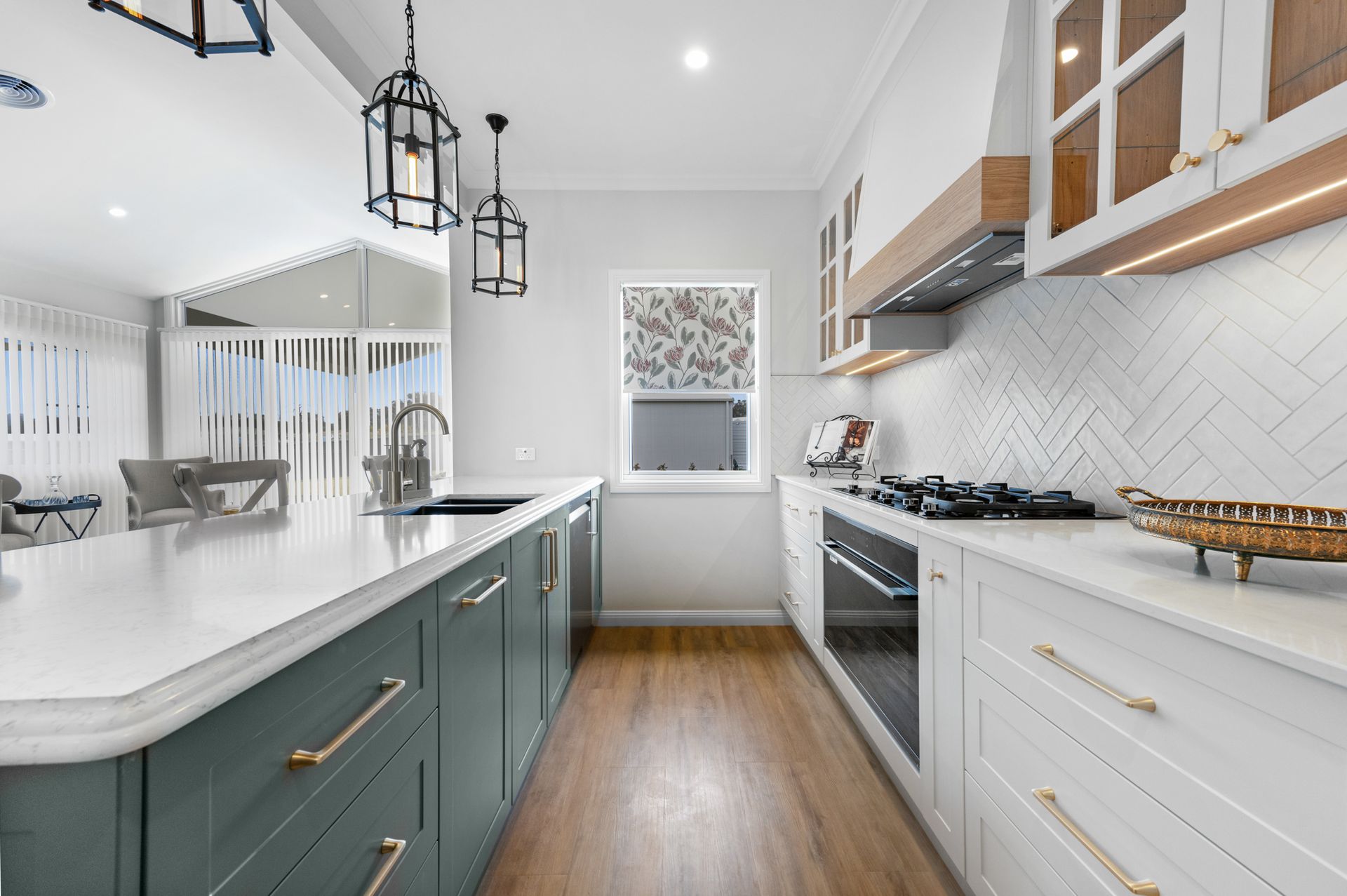 Bright modern kitchen with white cabinets, teal island, pendant lights, and wood floors