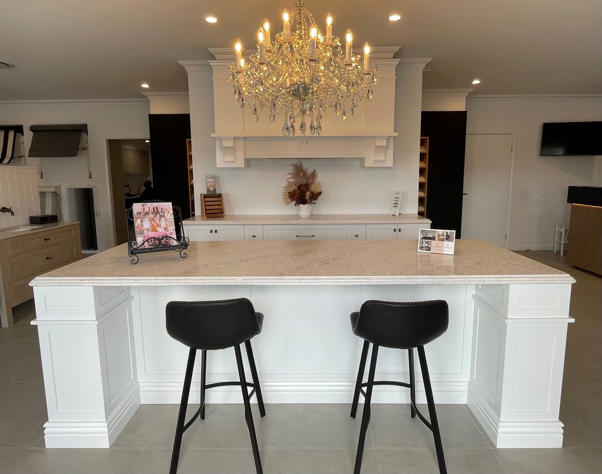 Modern kitchen with white island, two black stools, and a chandelier over the counter