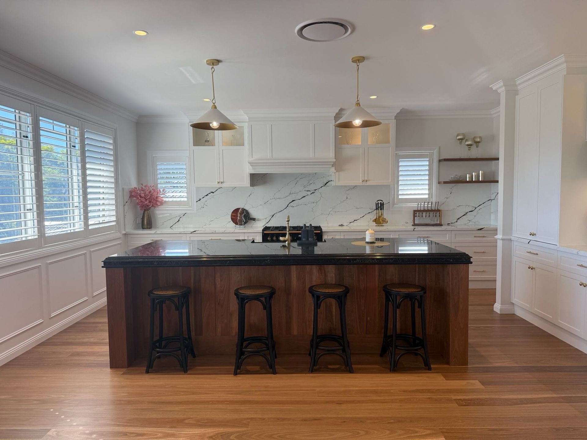 Bright white kitchen with dark island, three stools, pendant lights, and hardwood floors