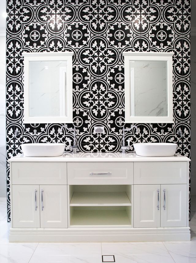 White double vanity with mirrors against black-and-white patterned tile wall in a bathroom